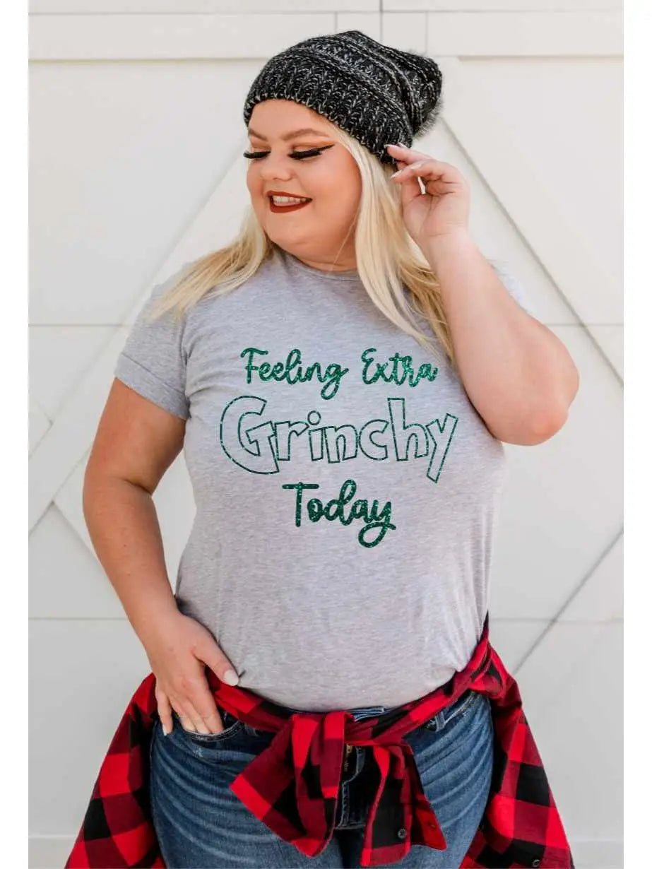 A person wearing a gray graphic tee with the text 'Feeling Extra Grinchy Today'.