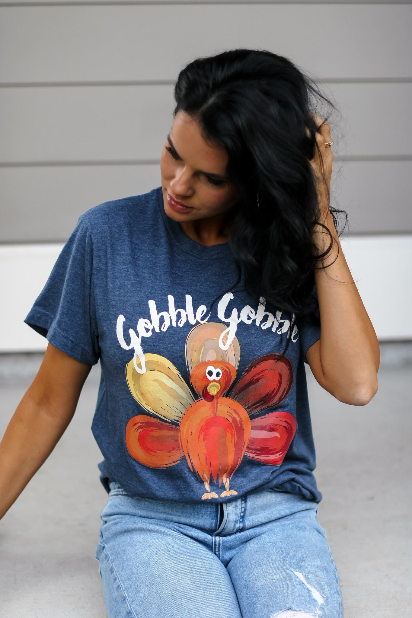 A woman wearing a blue heather denim t-shirt with 'Gobble Gobble' printed on it and a turkey graphic design.
