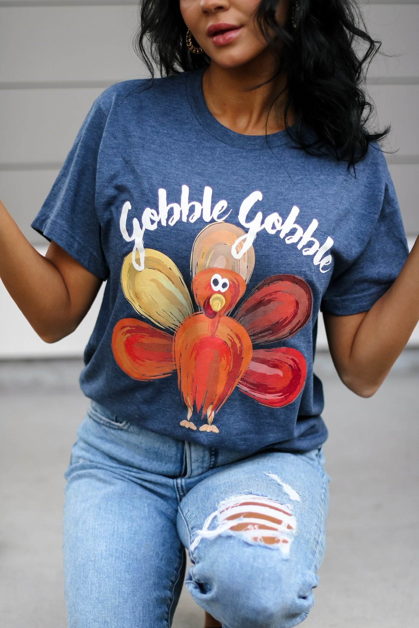 A woman wearing a blue heather denim t-shirt with 'Gobble Gobble' printed on it and a turkey graphic design.