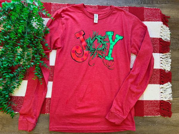 a red long sleeve graphic tee with the word 'JOY' printed on the front with Christmas graphics.
