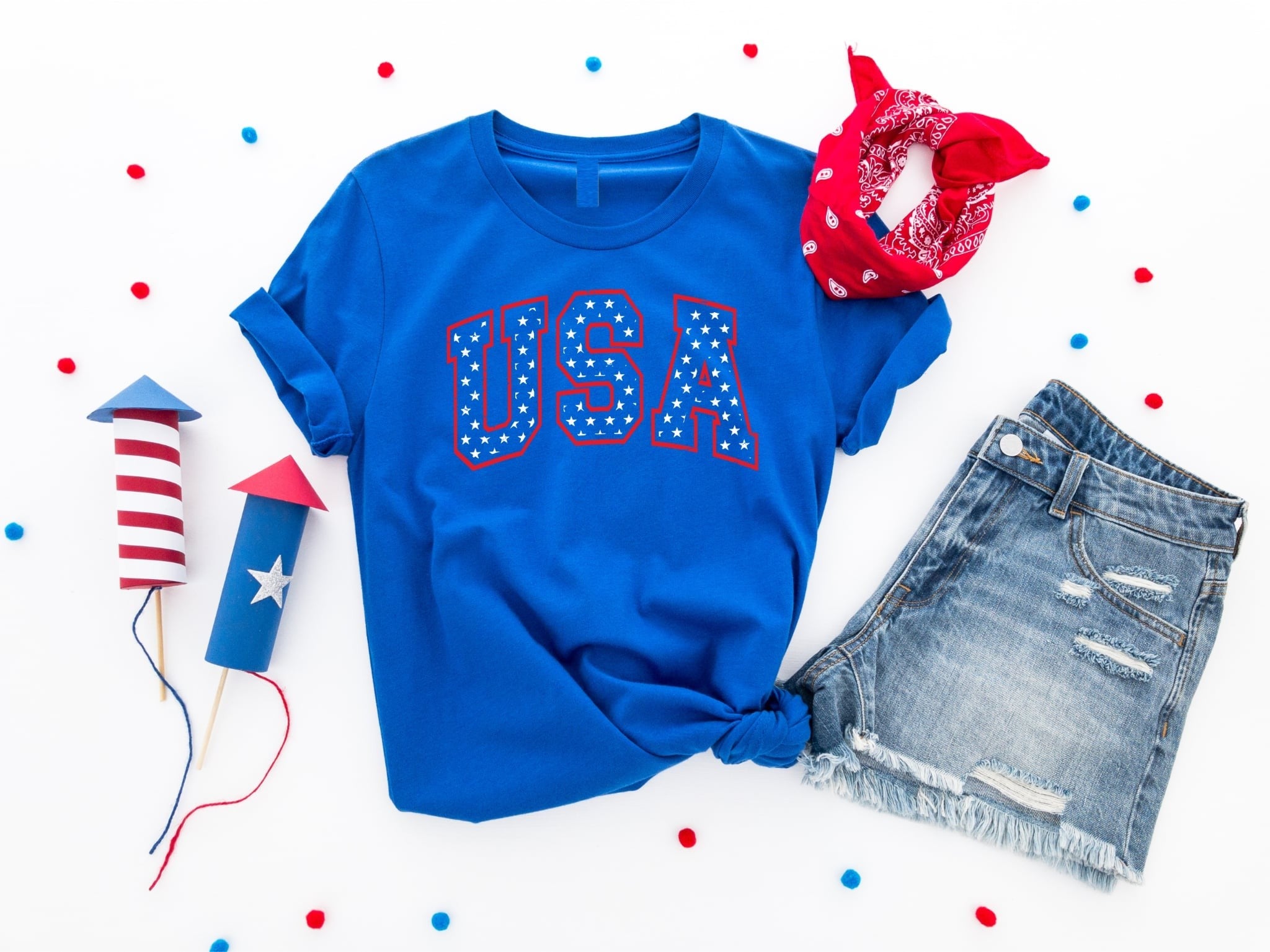 A royal blue graphic tee with 'USA' and stars design, accompanied by a pair of denim shorts and accessories with a patriotic theme.