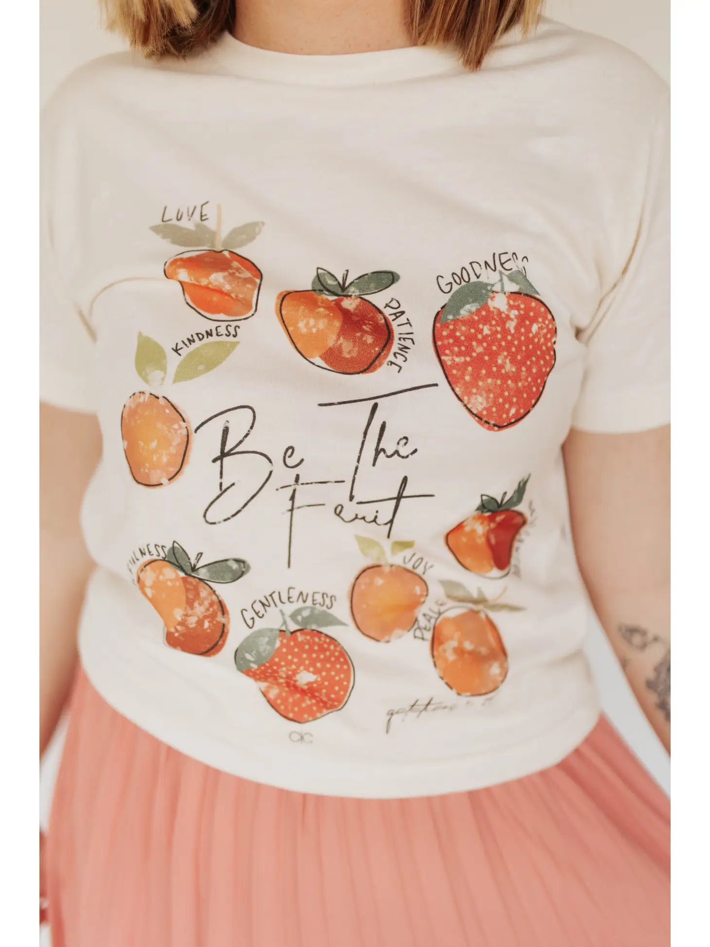 A person wearing a white graphic tee with fruit illustrations and the phrase 'Fruit of the Spirit' on it, Love, Kindness, Patience, Goodness, Joy, Peace, Gentleness, Self-Control and Faithfulness.' Galatians 5:22-23