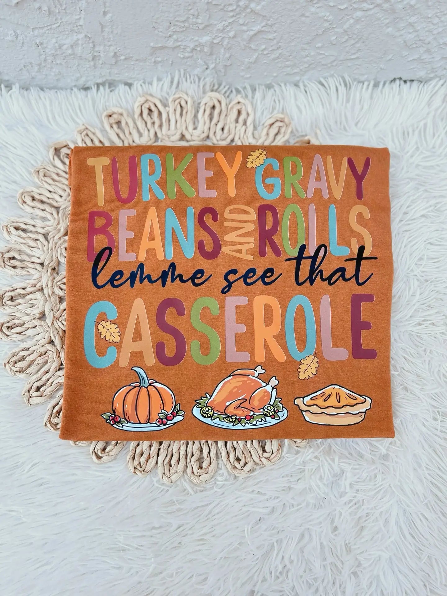 an orange t-shirt with Thanksgiving-themed text and graphics, that reads 'Turkey, gravy, beans and rolls, lemme see that casserole.'