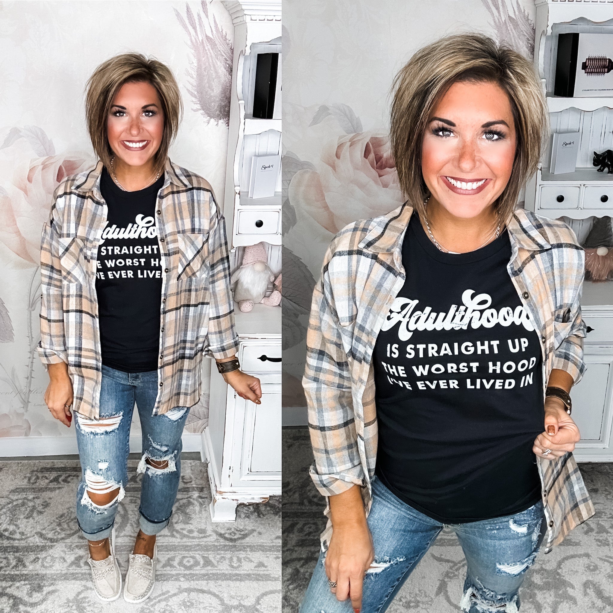 A women modeling a black graphic tee with the white text 'Adulthood Is Straight Up the Worst Hood I've Ever Lived in' on it.