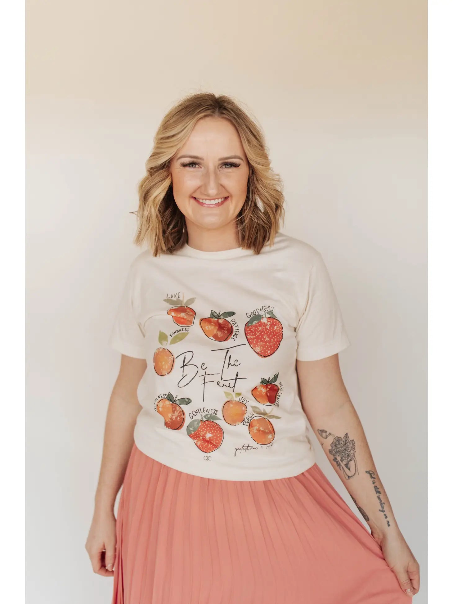 A person wearing a white graphic tee with fruit illustrations and the phrase 'Fruit of the Spirit' on it, Love, Kindness, Patience, Goodness, Joy, Peace, Gentleness, Self-Control and Faithfulness.' Galatians 5:22-23