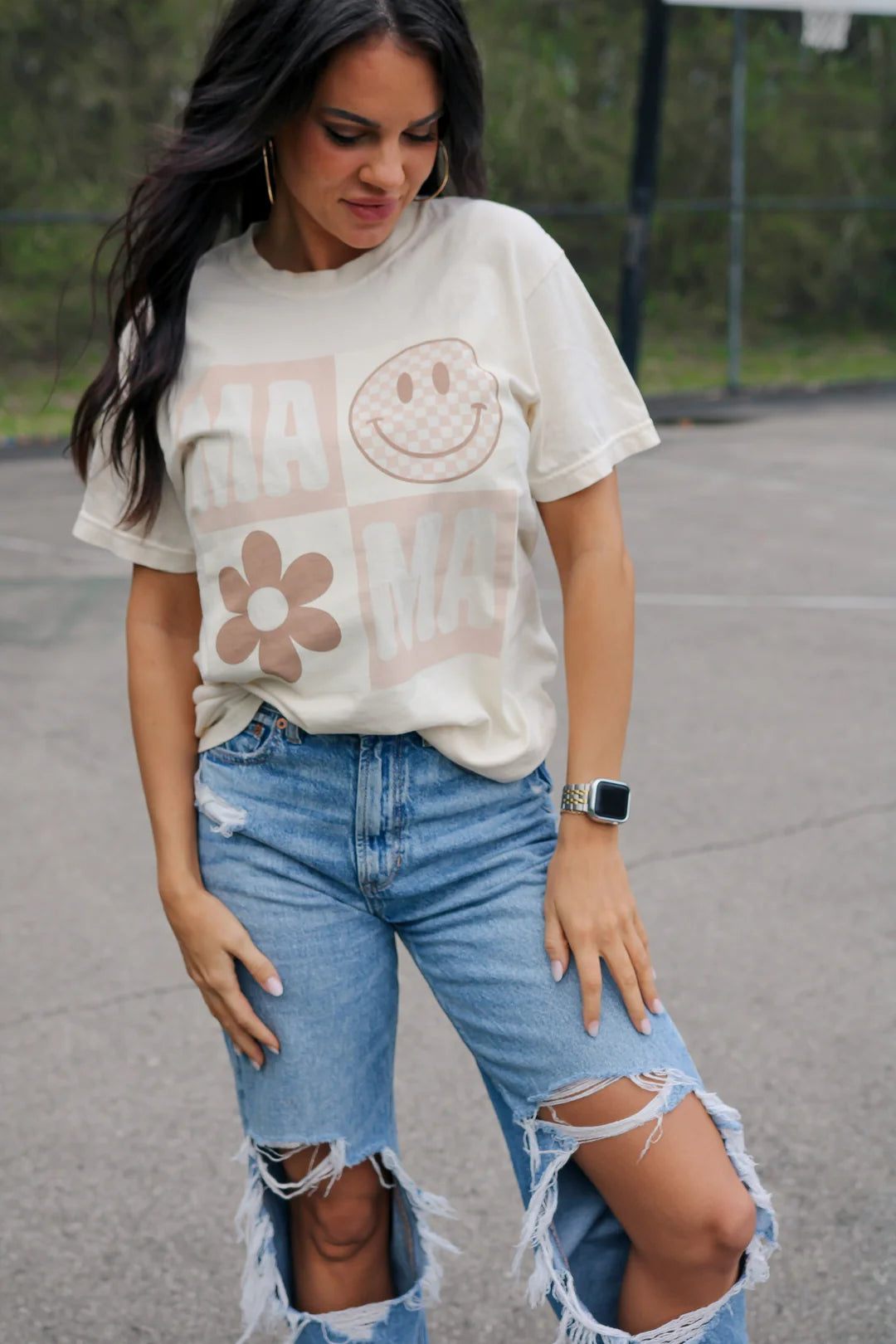 A woman wearing a cream crew-neck t-shirt with a smiley face graphic and text that reads 'MAMA'.