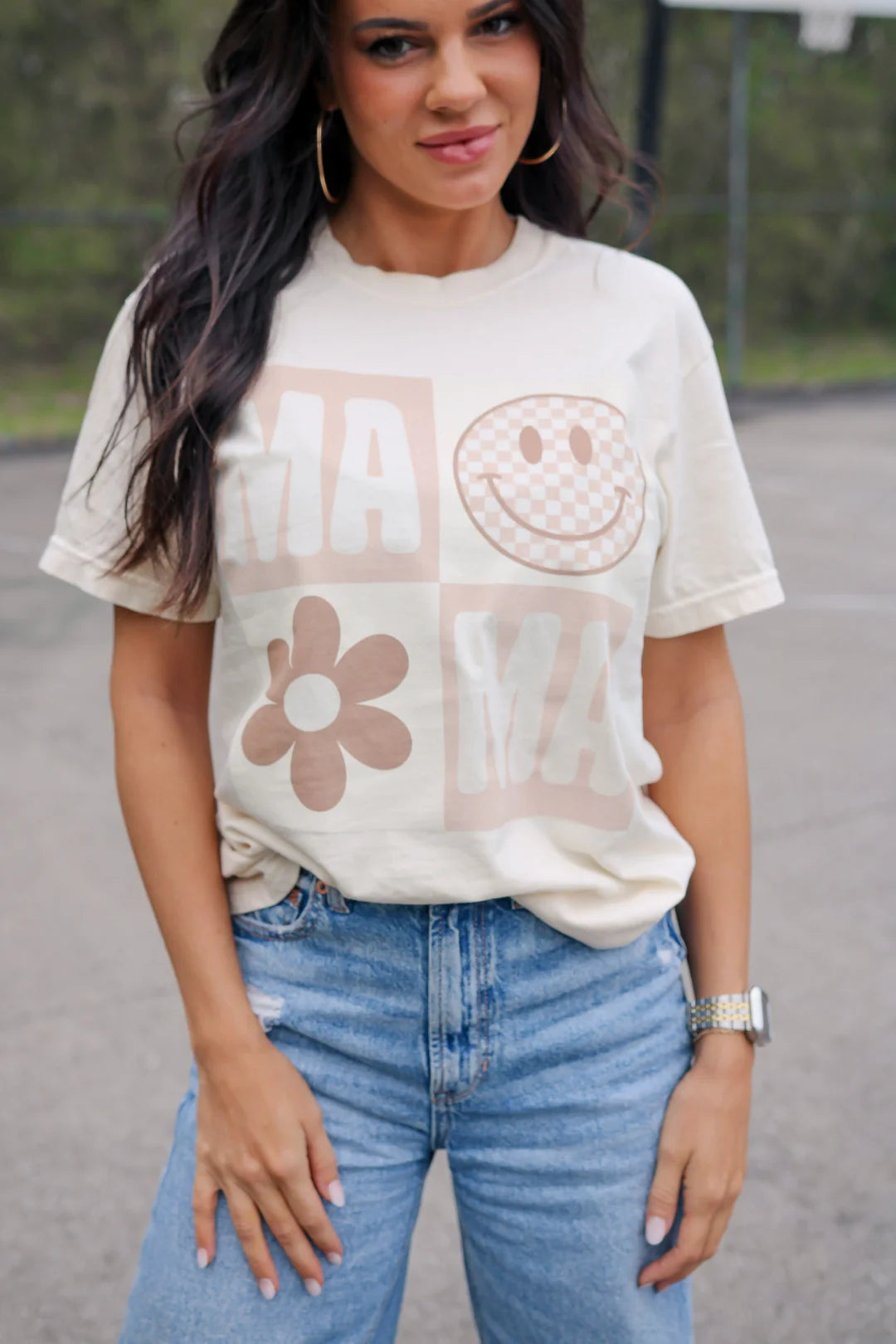 A woman wearing a cream crew-neck t-shirt with a smiley face graphic and text that reads 'MAMA'.