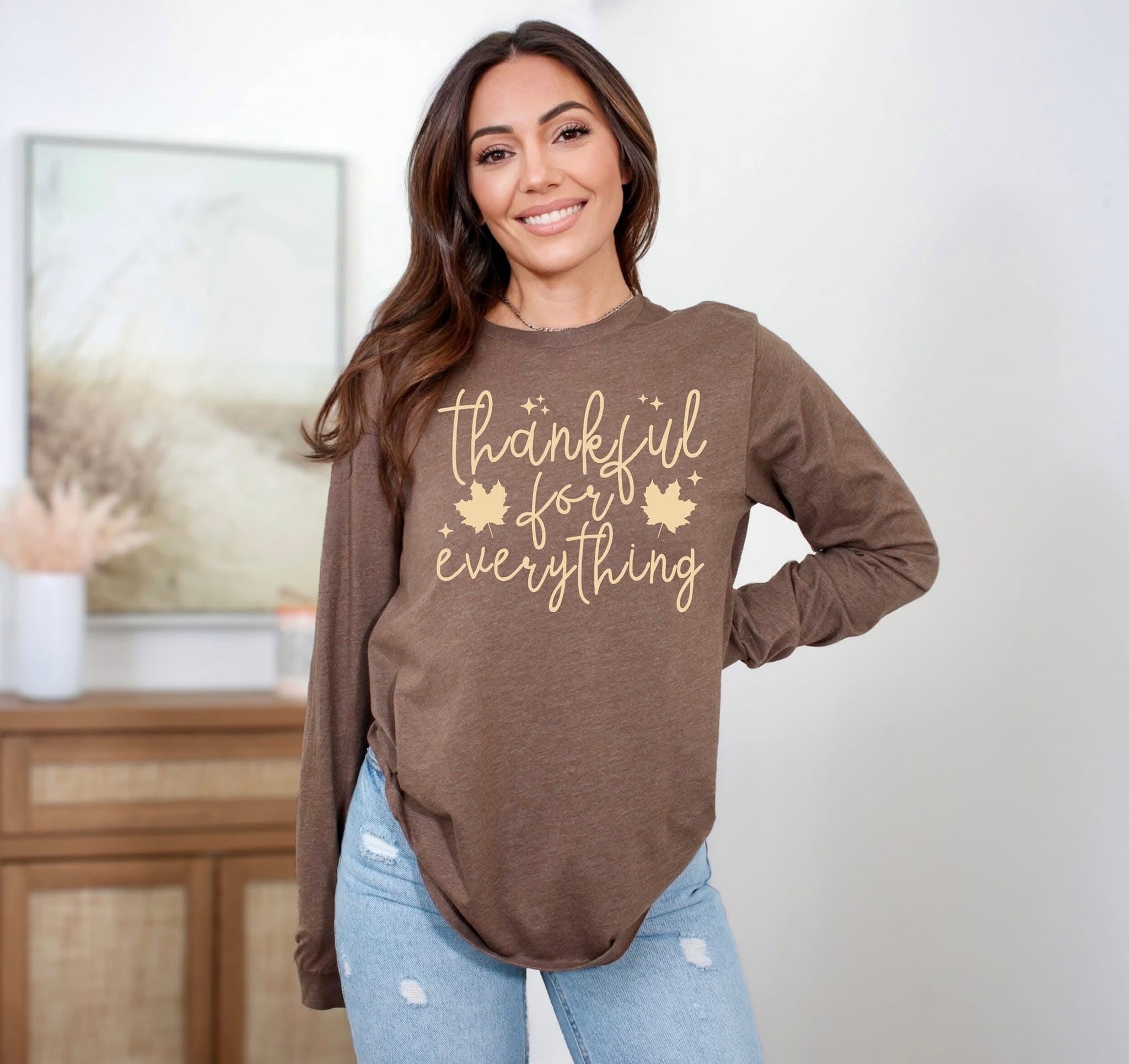 A woman wearing a brown long sleeve graphic tee that says 'thankful for everything' in pale yellow lettering.