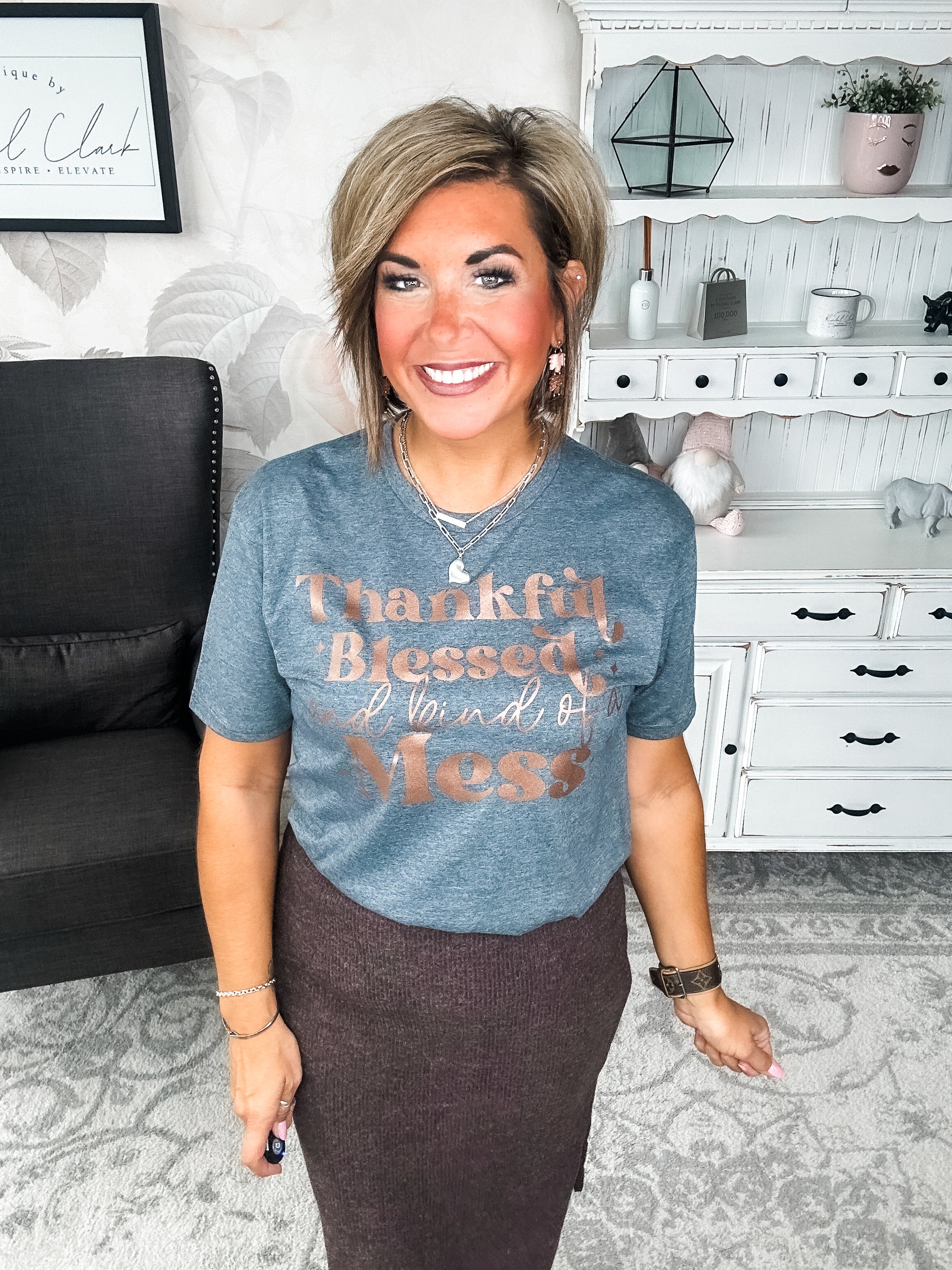 A woman wearing a grey t-shirt with the text 'Thankful Blessed and kind of a Mess' written in rose gold foil print.