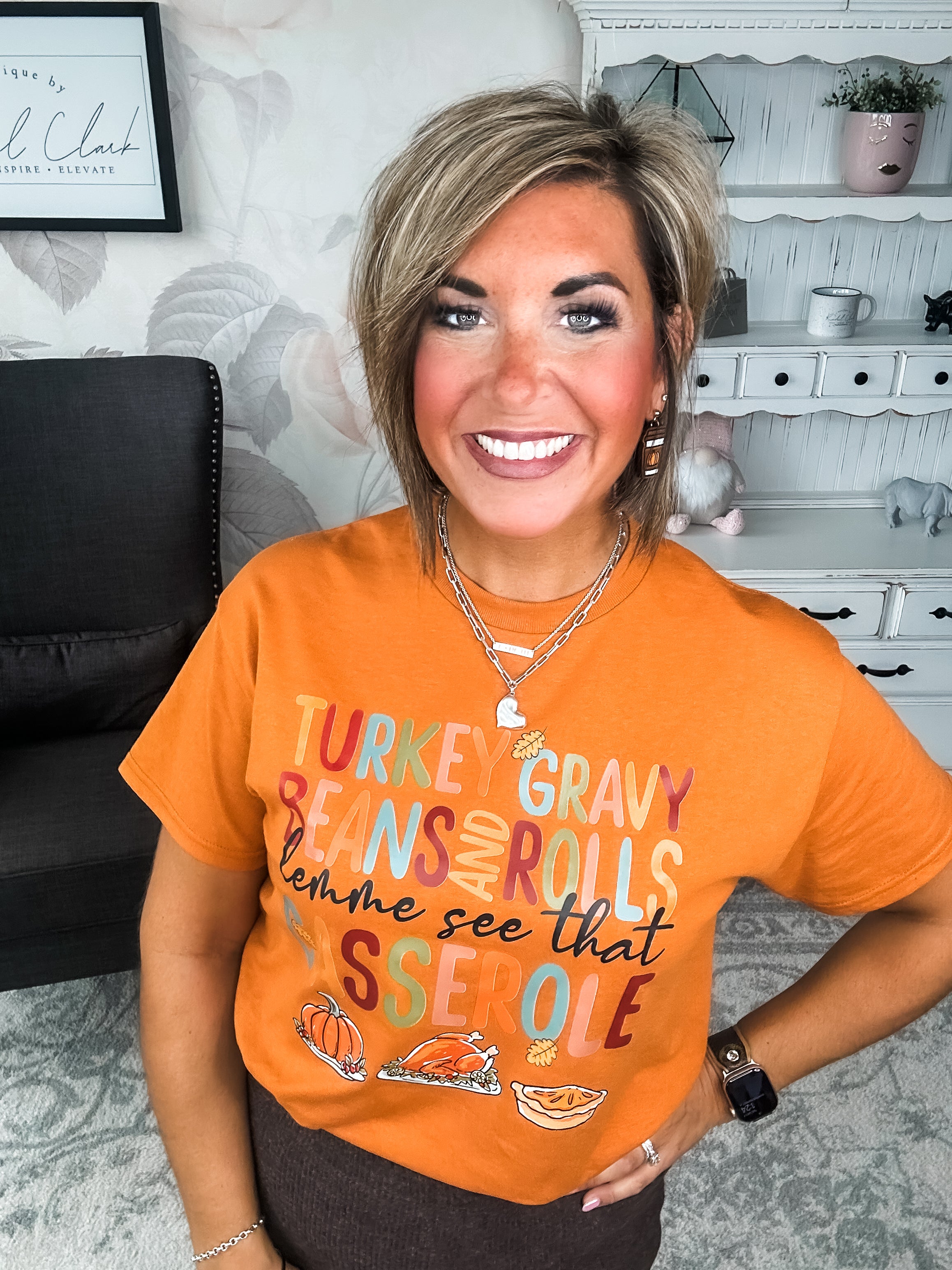 Woman wearing an orange t-shirt with Thanksgiving-themed text and graphics, that reads 'Turkey, gravy, beans and rolls, lemme see that casserole.'