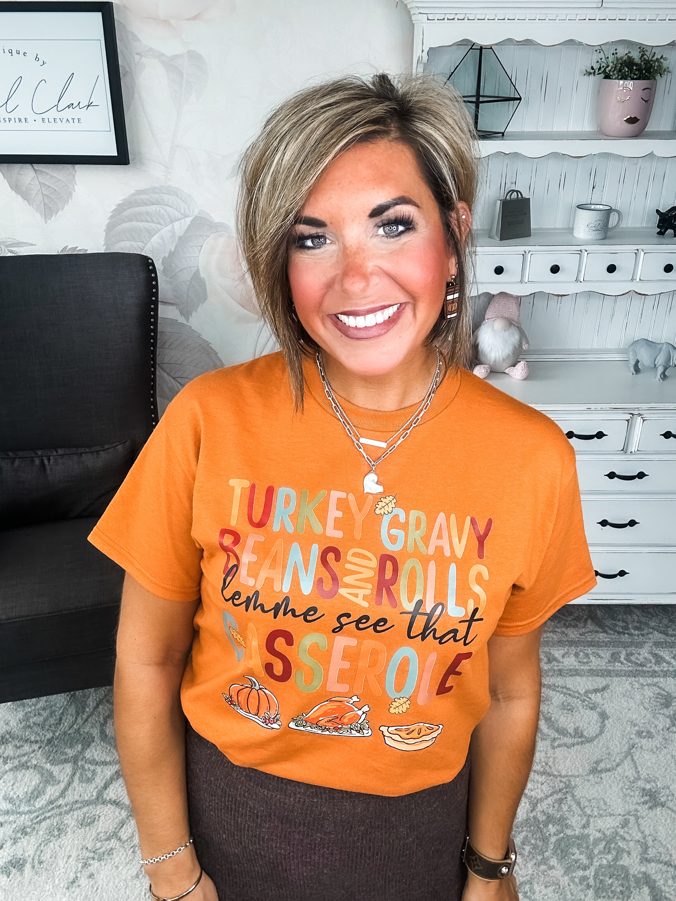 Woman wearing an orange t-shirt with Thanksgiving-themed text and graphics, that reads 'Turkey, gravy, beans and rolls, lemme see that casserole.'