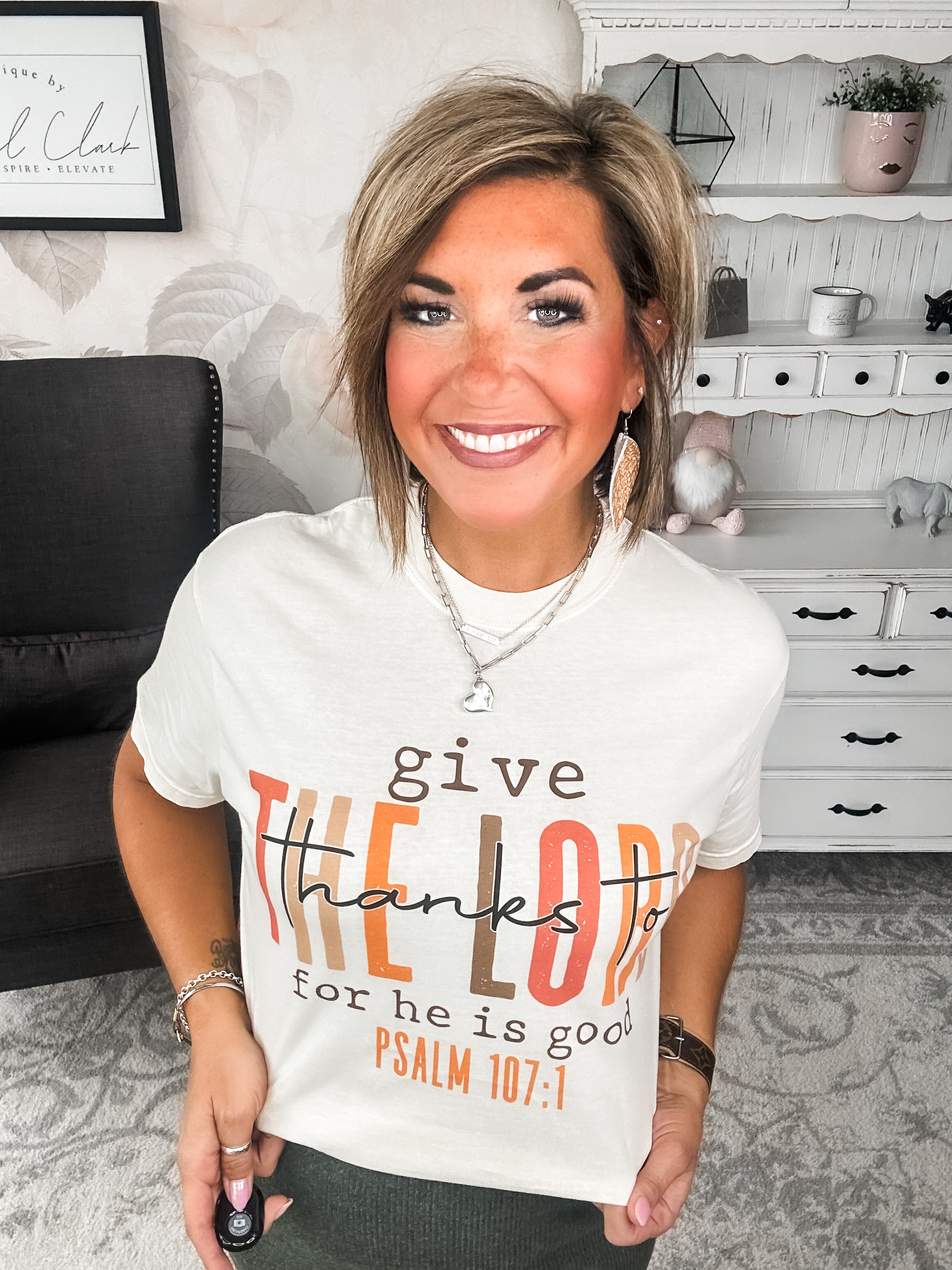 Woman wearing a cream t-shirt that reads 'give thanks to the Lord for he is good. Psalm 107:1'