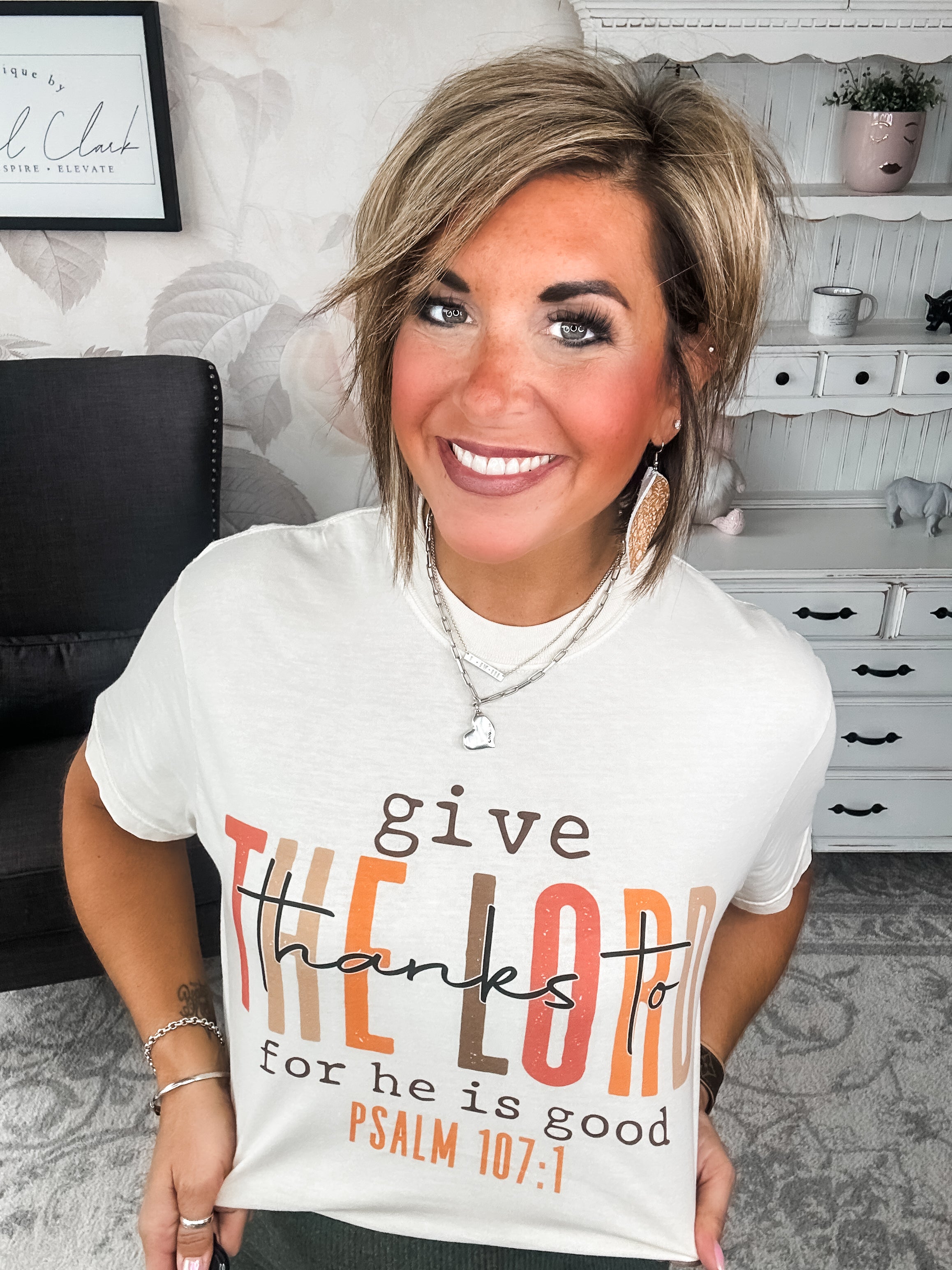 Woman wearing a cream t-shirt that reads 'give thanks to the Lord for he is good. Psalm 107:1'