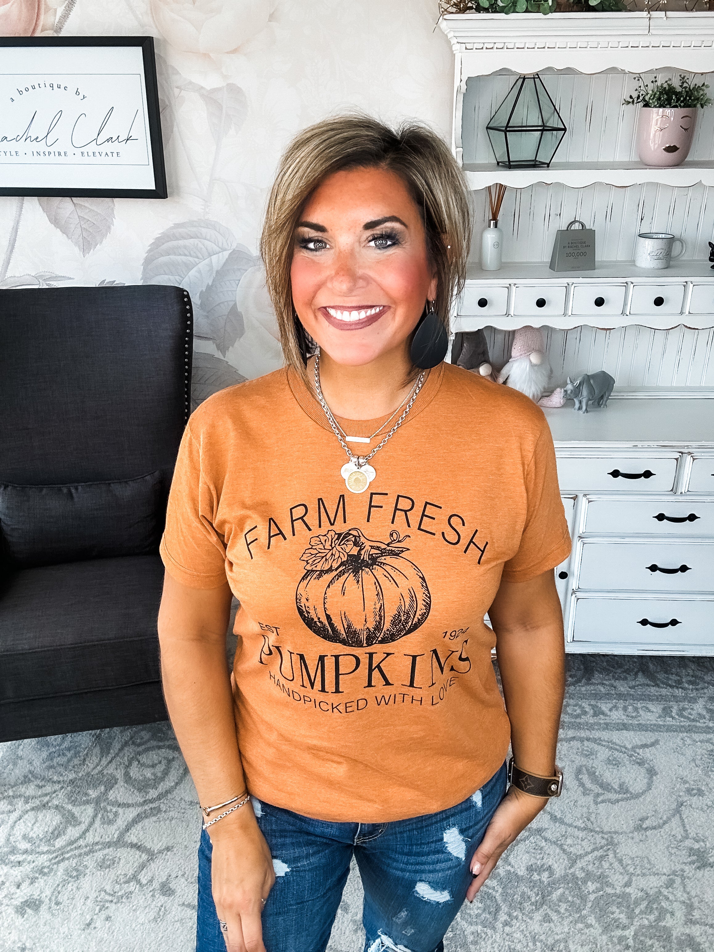 Woman wearing an orange t-shirt that says 'Farm Fresh Pumpkins, Handpicked with Love, Est. 1924' with a pumpkin graphic.