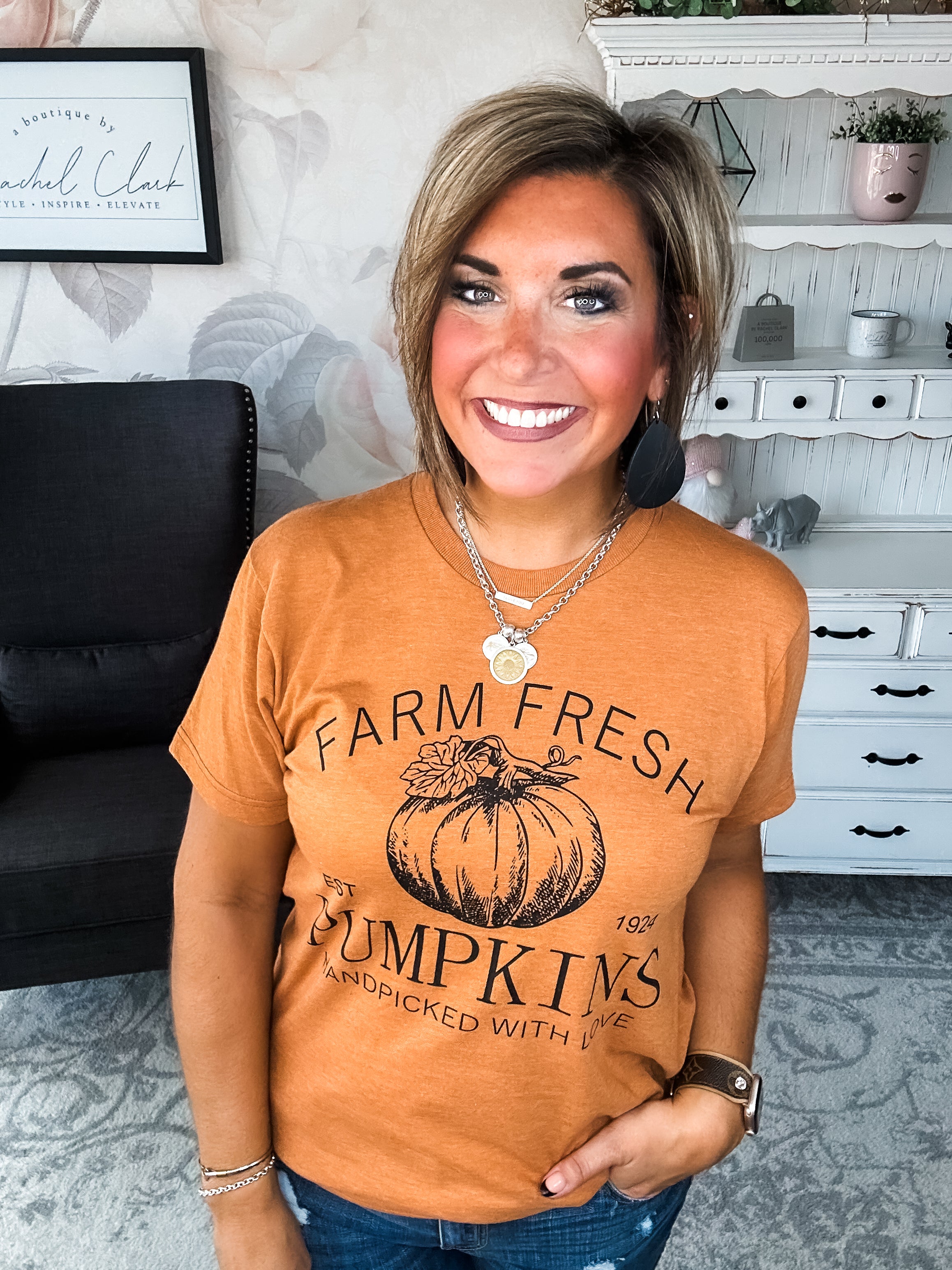Woman wearing an orange t-shirt that says 'Farm Fresh Pumpkins, Handpicked with Love, Est. 1924' with a pumpkin graphic.