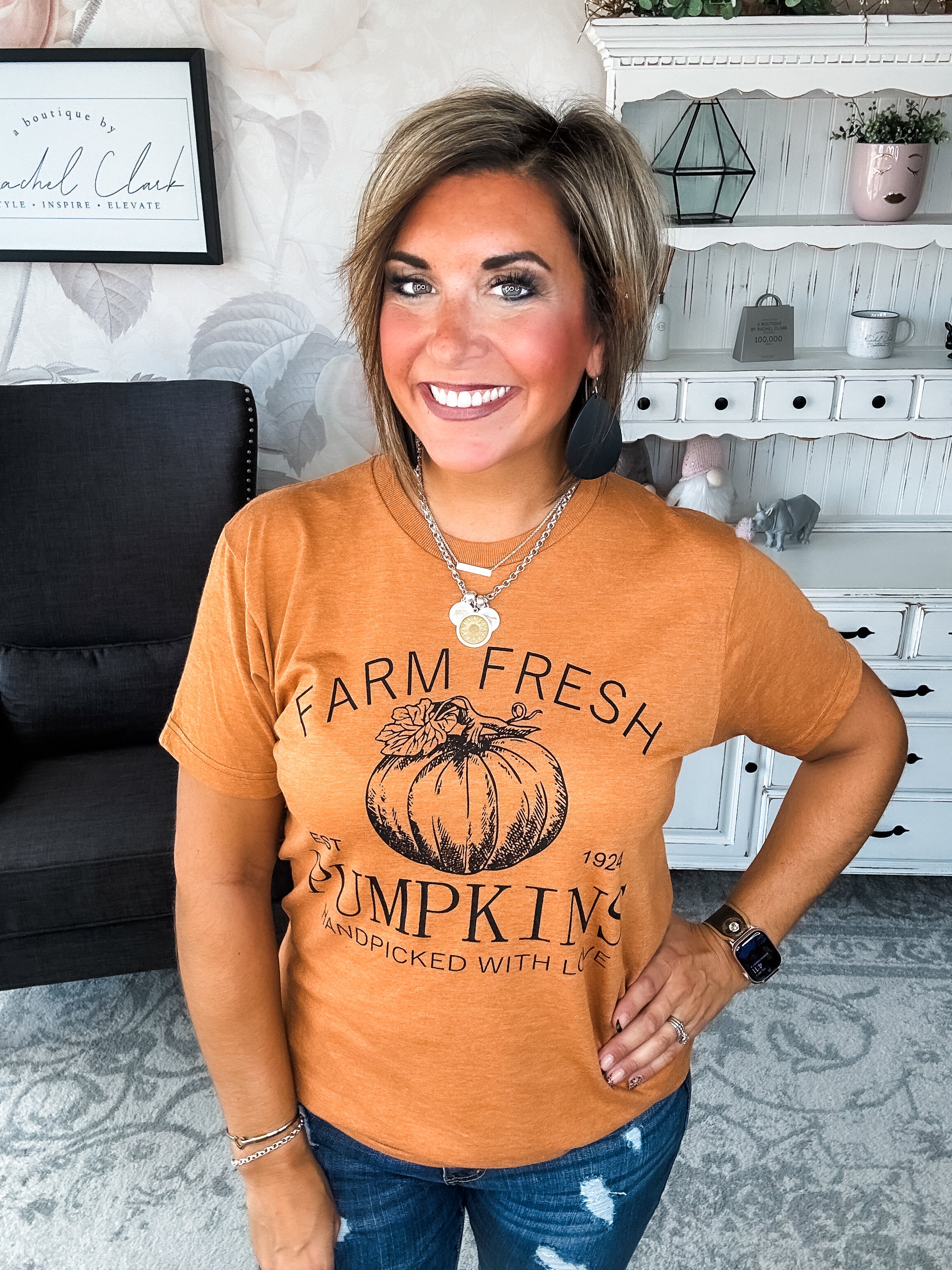 Woman wearing an orange t-shirt that says 'Farm Fresh Pumpkins, Handpicked with Love, Est. 1924' with a pumpkin graphic.
