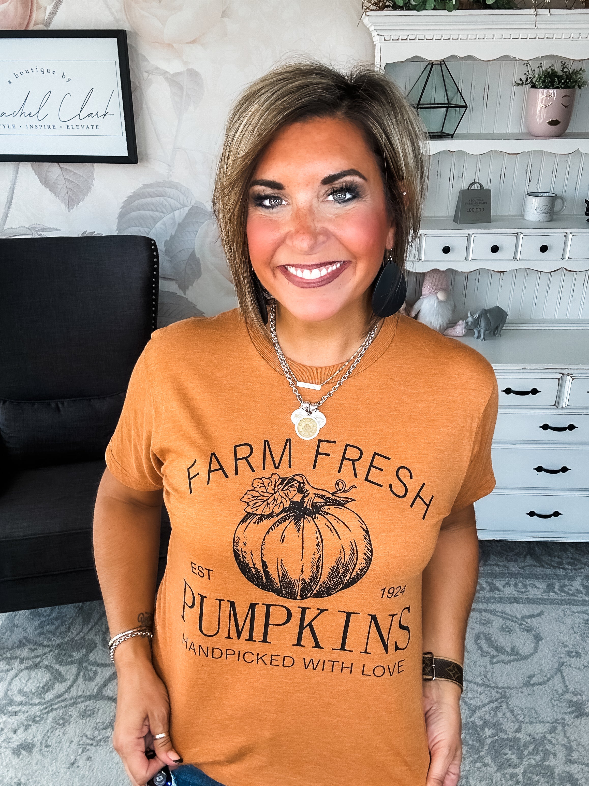 Woman wearing an orange t-shirt that says 'Farm Fresh Pumpkins, Handpicked with Love, Est. 1924' with a pumpkin graphic.