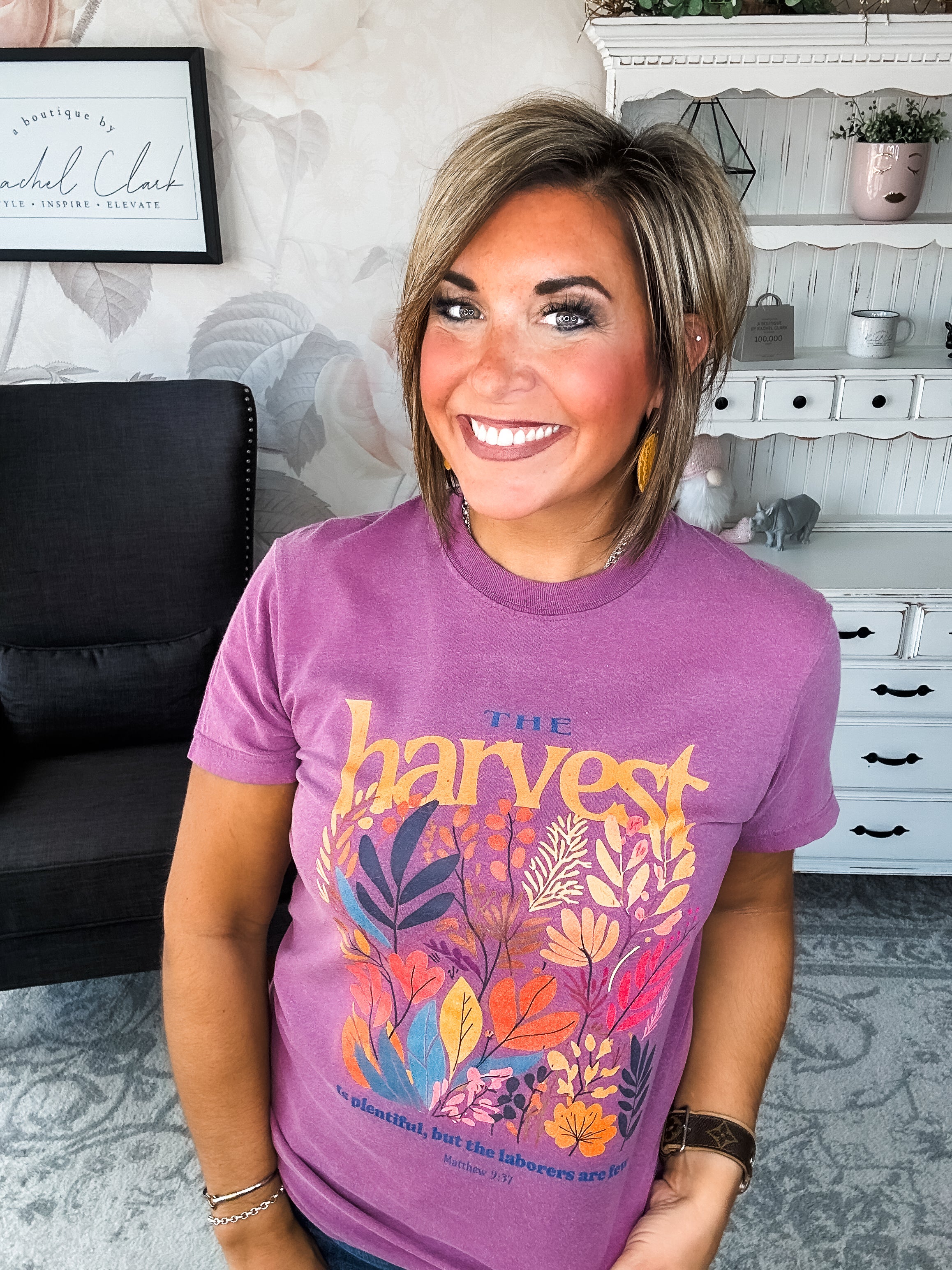 Woman wearing a purple t-shirt with floral designs that reads 'The Harvest is Plentiful, but the Laborers are Few, Matthew 9:37'