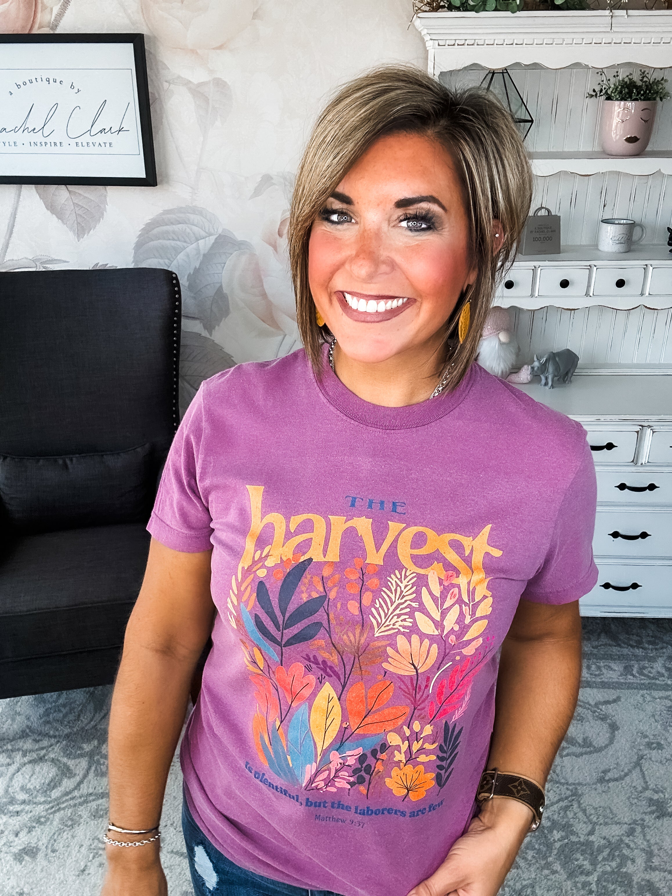 Woman wearing a purple t-shirt with floral designs that reads 'The Harvest is Plentiful, but the Laborers are Few, Matthew 9:37'
