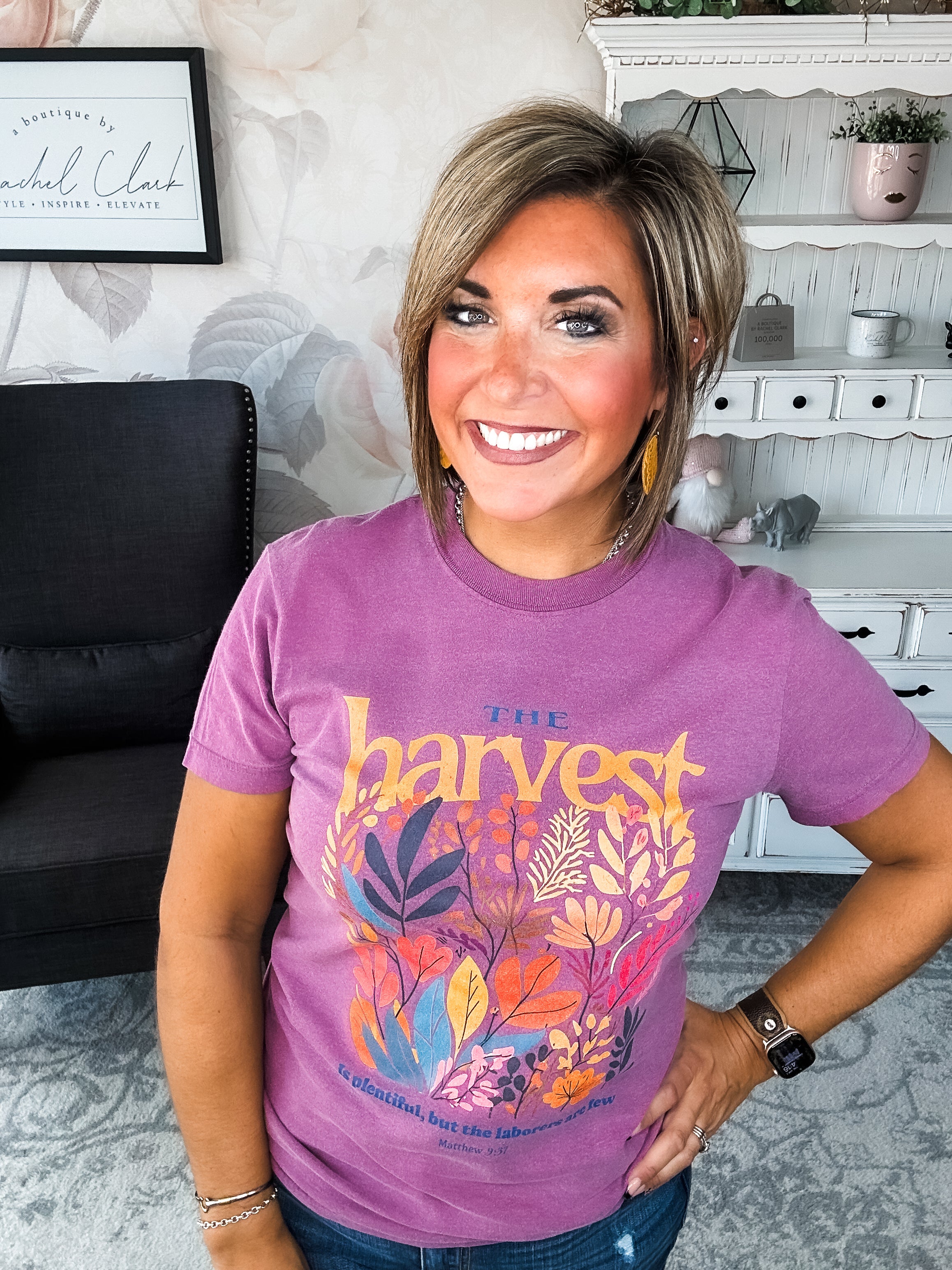 Woman wearing a purple t-shirt with floral designs that reads 'The Harvest is Plentiful, but the Laborers are Few, Matthew 9:37'