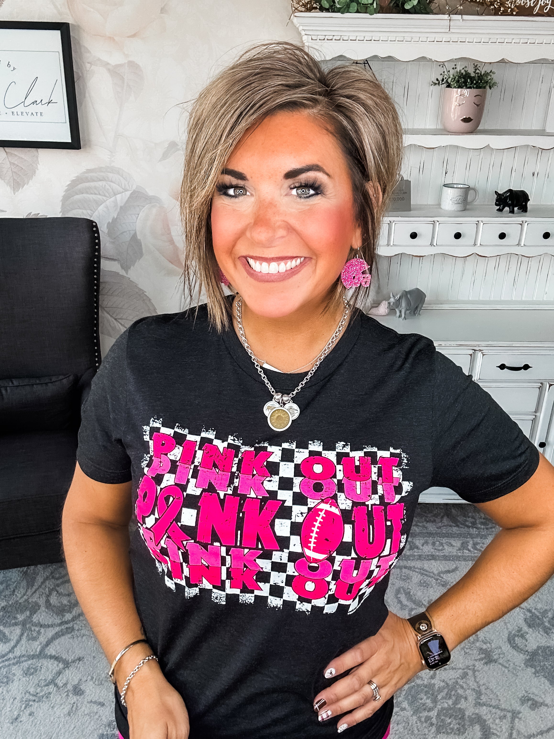 Woman wearing a black t-shirt with pink text that reads 'Pink Out' repeatedly with a football graphic.