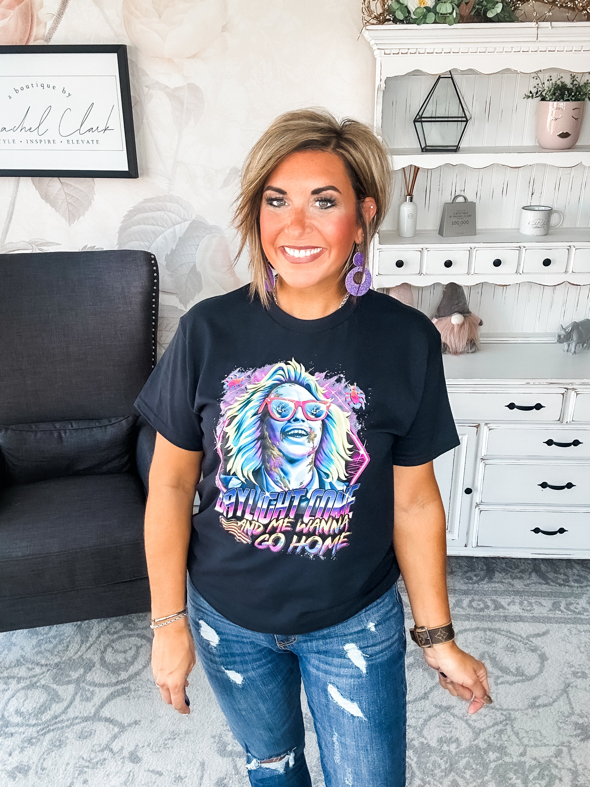 Woman wearing a black t-shirt with colorful graphic design that reads 'Daylight Come and Me Wanna Go Home.'