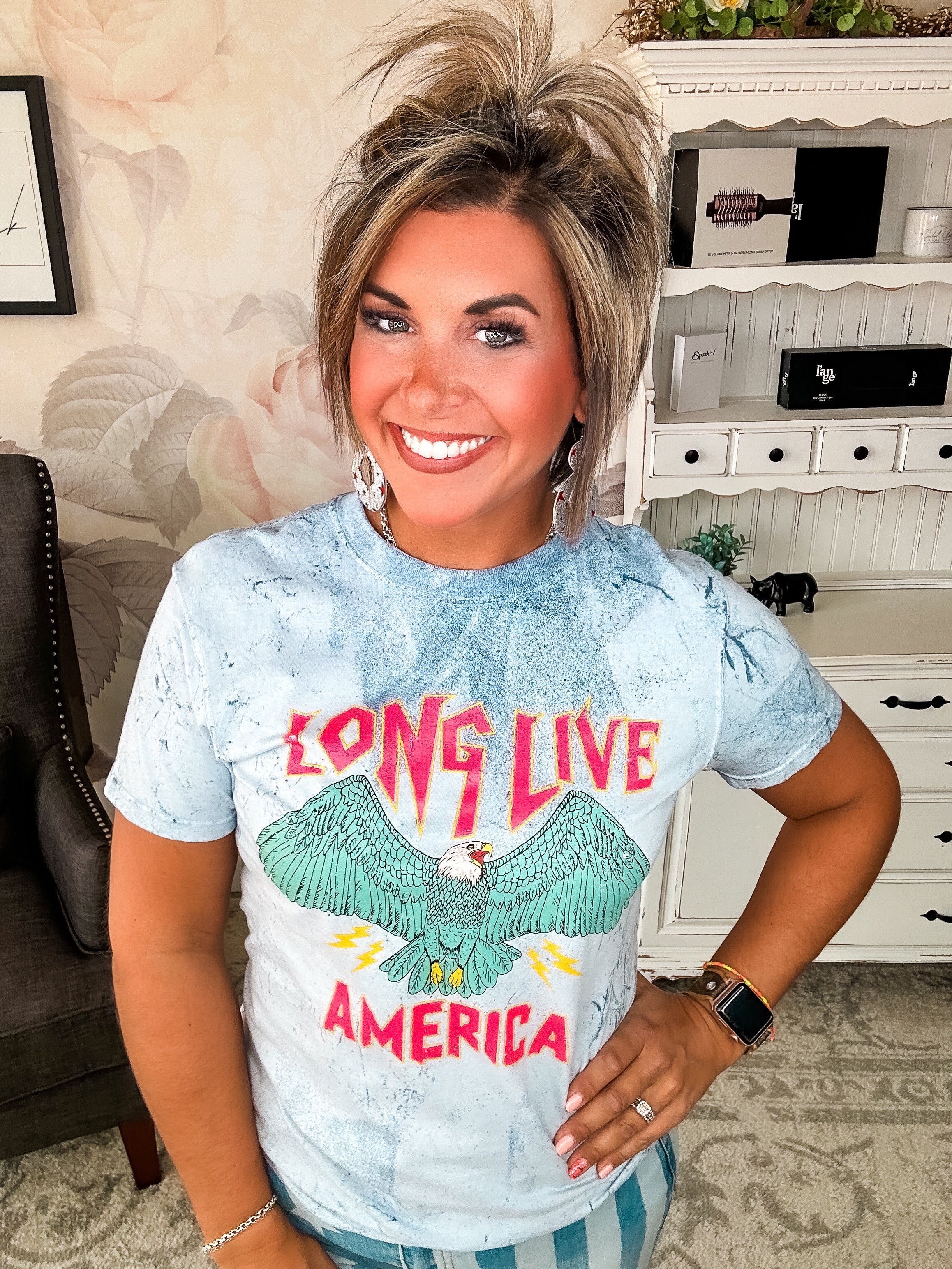 A person wearing a crew-neck, short-sleeve graphic tee with the phrase 'LONG LIVE AMERICA' printed on it, in a bleached blue color.