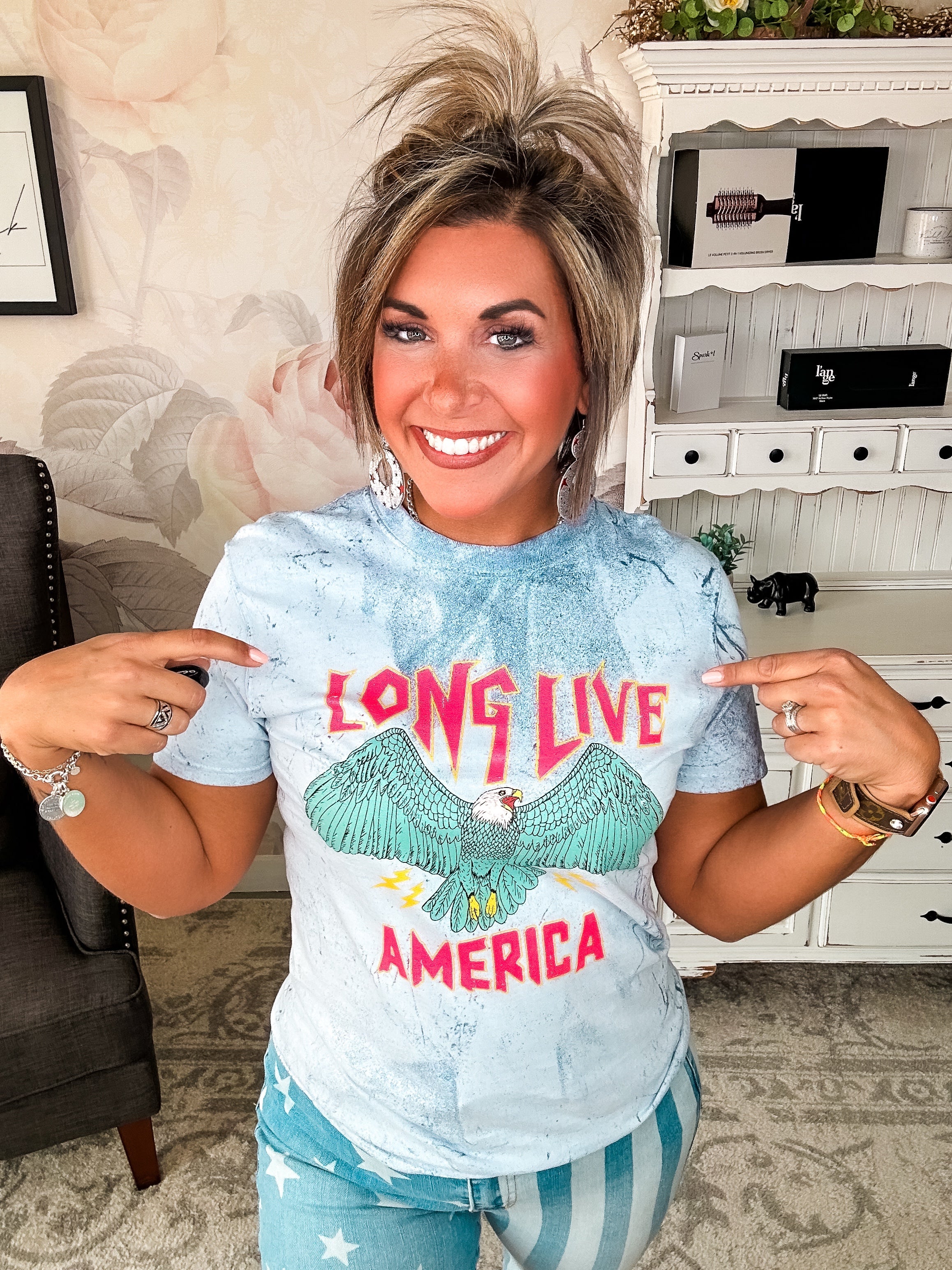 A person wearing a crew-neck, short-sleeve graphic tee with the phrase 'LONG LIVE AMERICA' printed on it, in a bleached blue color.