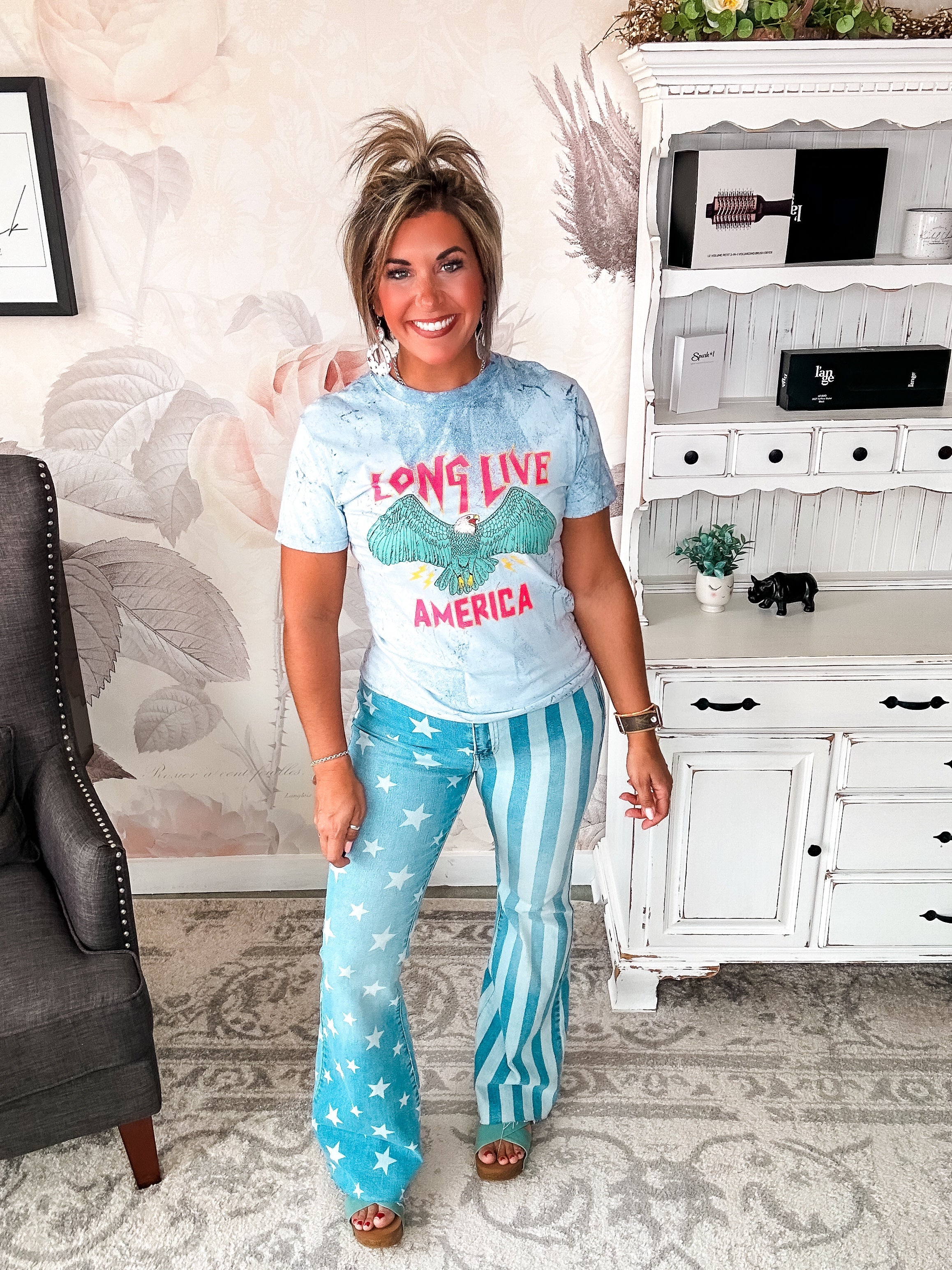 A person wearing a crew-neck, short-sleeve graphic tee with the phrase 'LONG LIVE AMERICA' printed on it, in a bleached blue color.