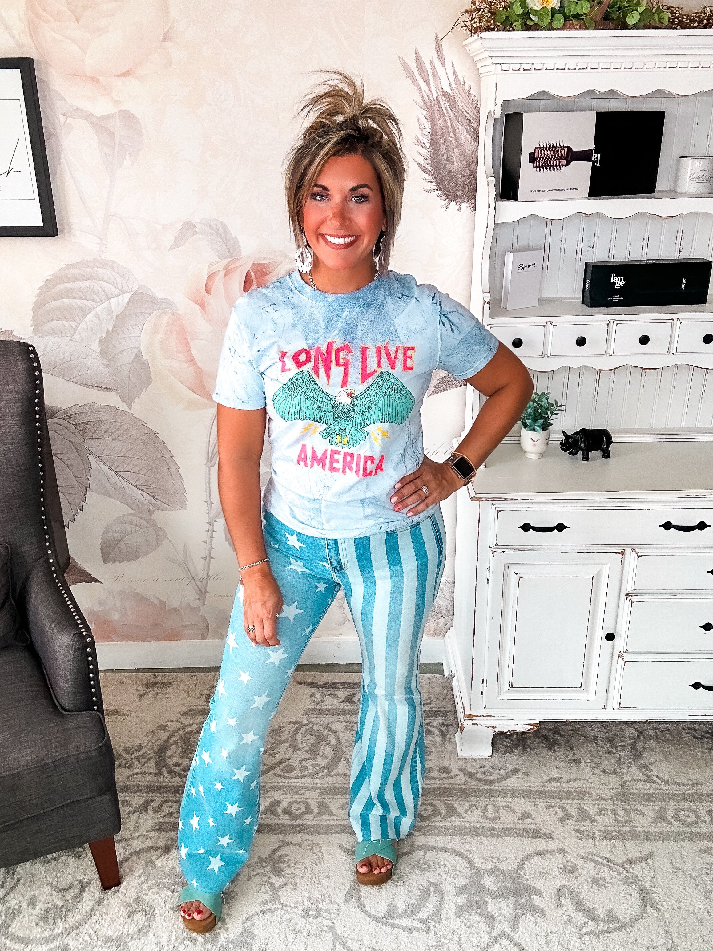 A person wearing a crew-neck, short-sleeve graphic tee with the phrase 'LONG LIVE AMERICA' printed on it, in a bleached blue color.