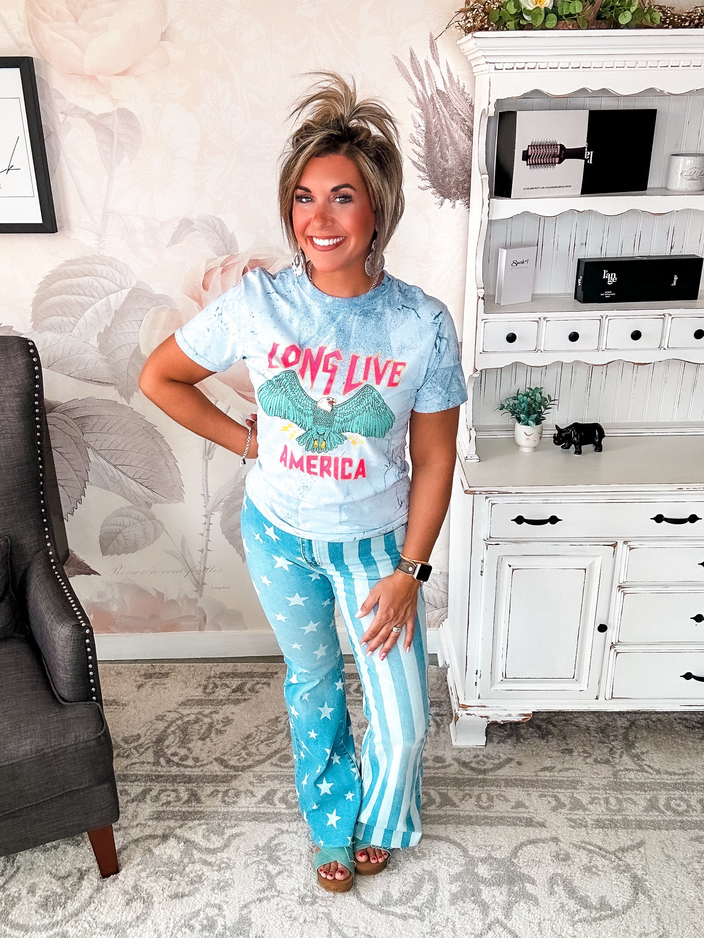 A person wearing a crew-neck, short-sleeve graphic tee with the phrase 'LONG LIVE AMERICA' printed on it, in a bleached blue color.