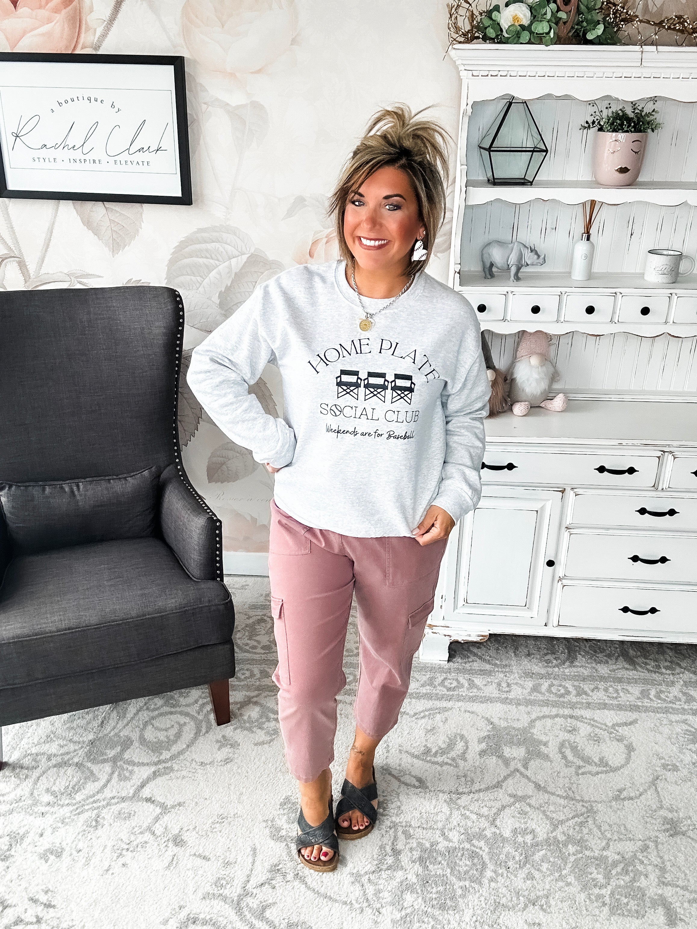 A woman wearing a gray pullover sweatshirt with the text 'HOME PLATE SOCIAL CLUB. Weekends are for Baseball'