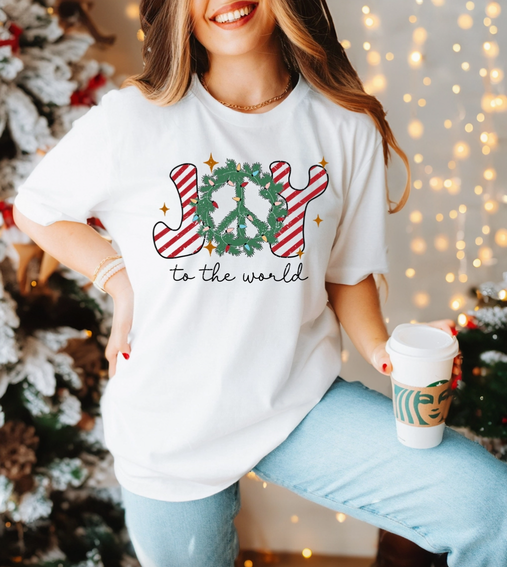 A woman wearing a white graphic tee with a Christmas wreath and the text 'Joy to the World' on it.
