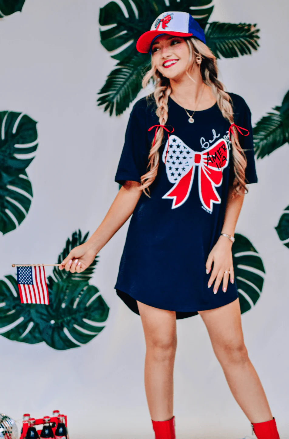 A woman wearing a navy t-shirt dress with a large bow graphic on the front and small text that reads 'God Bless America'.
