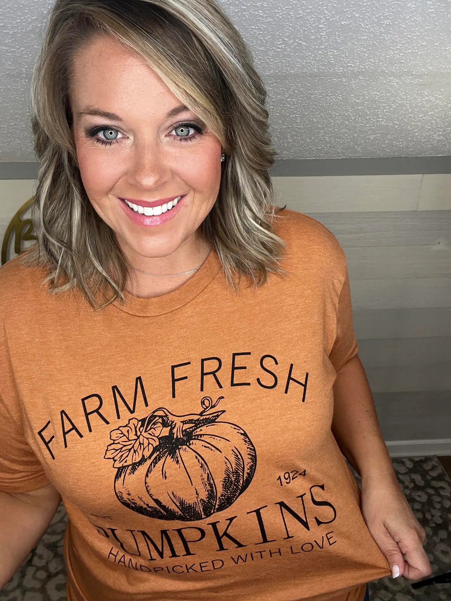 Woman wearing an orange t-shirt that says 'Farm Fresh Pumpkins, Handpicked with Love, Est. 1924' with a pumpkin graphic.