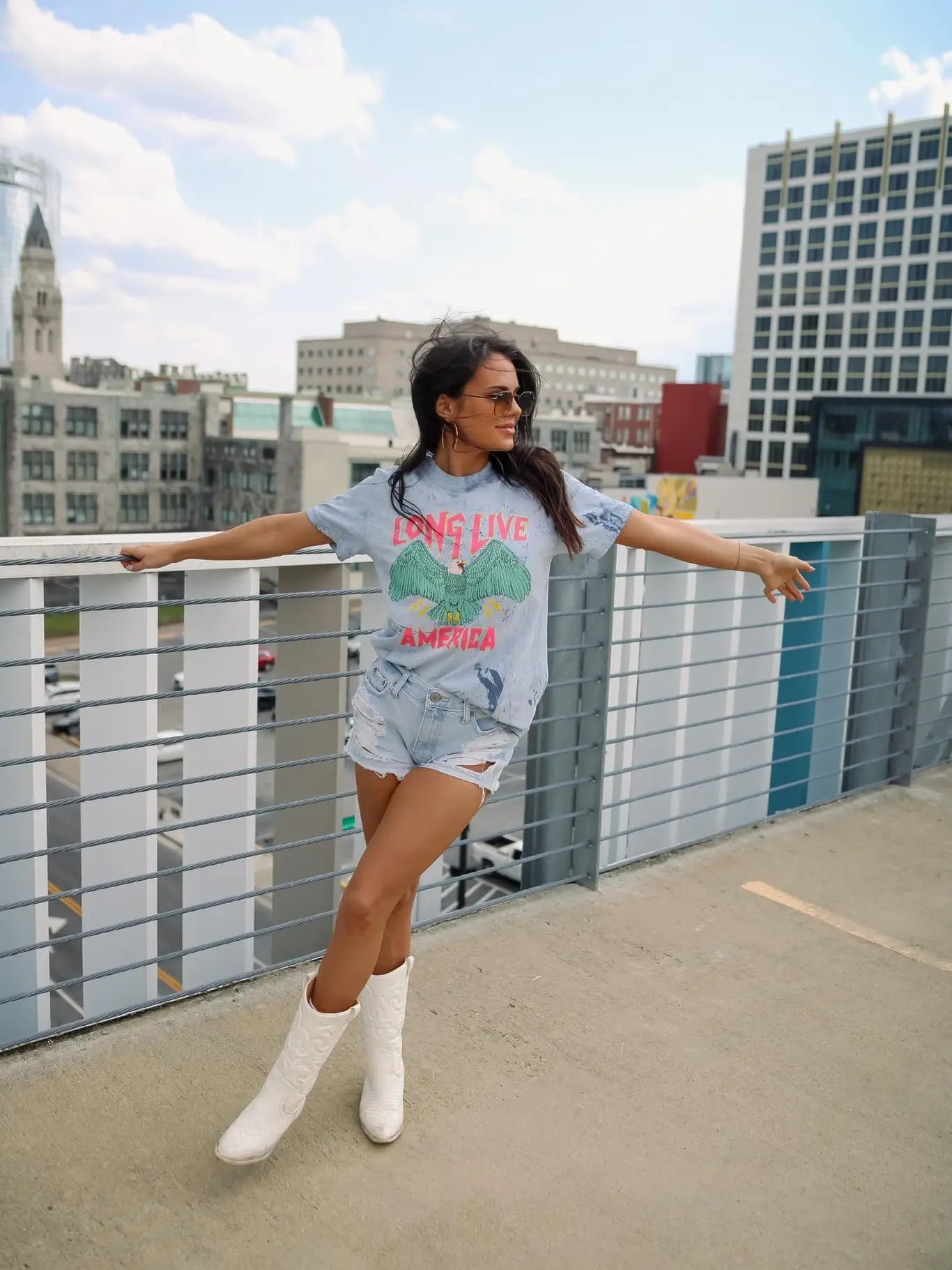 A person wearing a crew-neck, short-sleeve graphic tee with the phrase 'LONG LIVE AMERICA' printed on it, in a bleached blue color.
