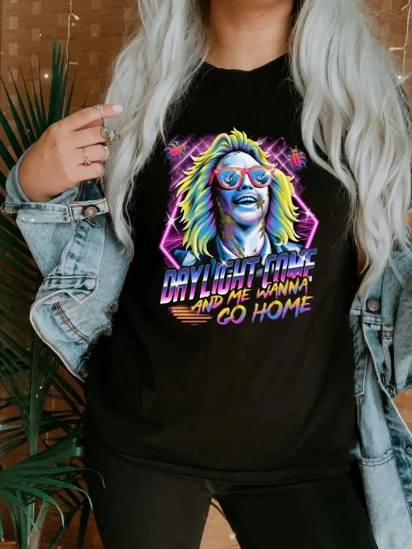 Woman wearing a black t-shirt with colorful graphic design that reads 'Daylight Come and Me Wanna Go Home.'