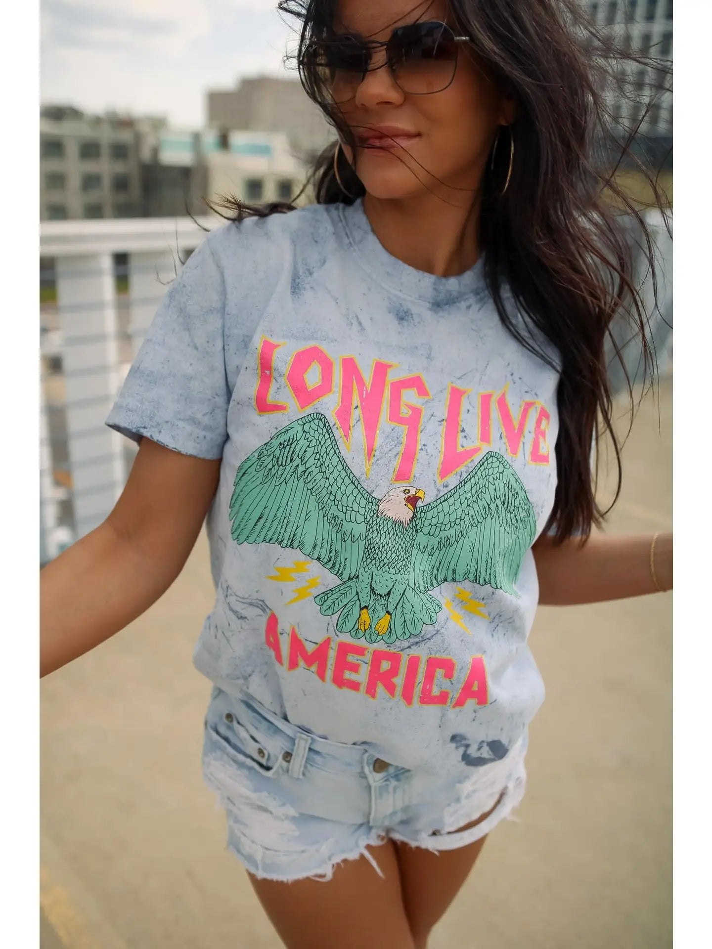 A person wearing a crew-neck, short-sleeve graphic tee with the phrase 'LONG LIVE AMERICA' printed on it, in a bleached blue color.