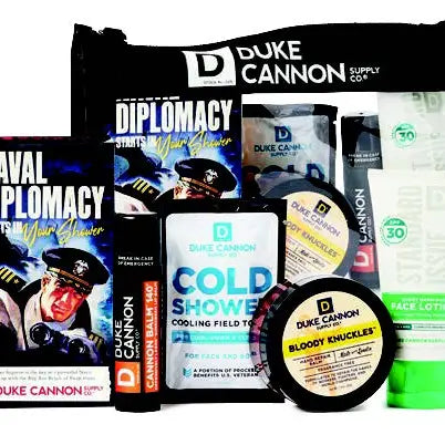 A gift set by Duke Cannon including various grooming products such as soap, a towel, lip protectant, hand repair balm, and face lotion, packed in a travel bag.