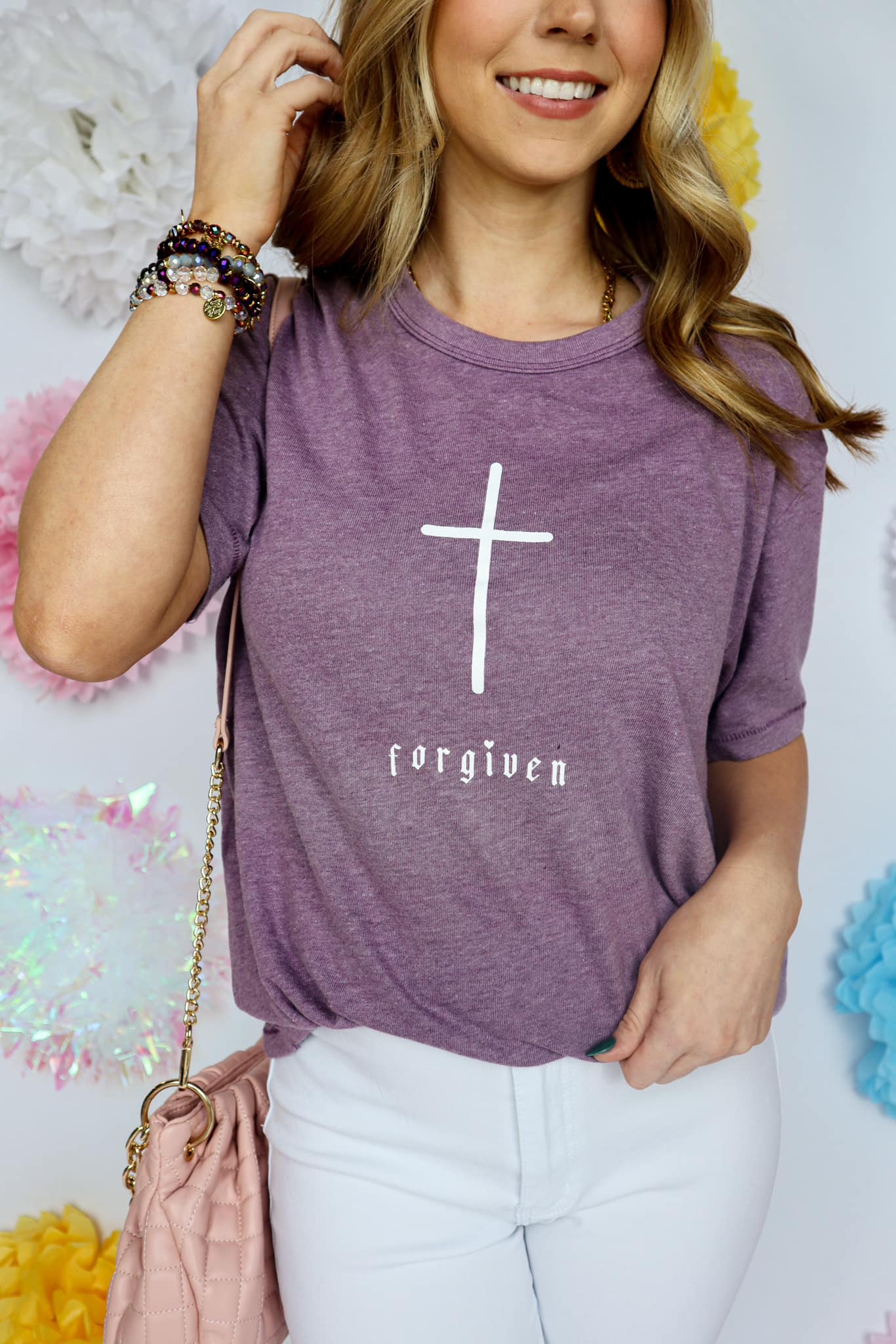 A woman wearing a purple graphic tee with a cross and the word 'forgiven' printed on the front.