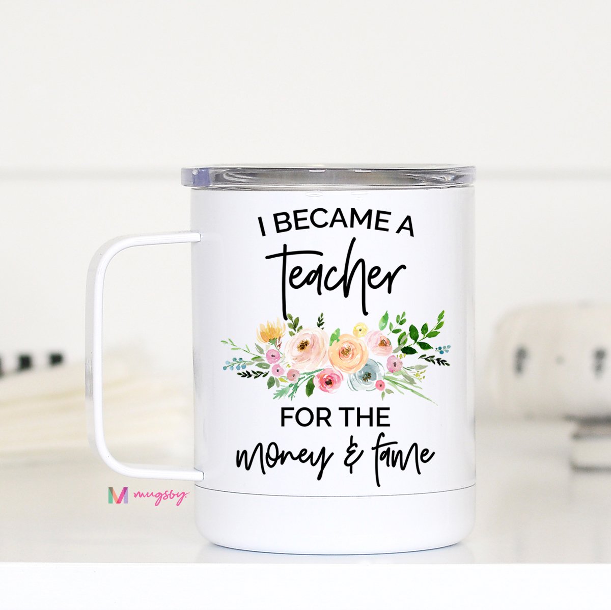 A white stainless steel travel mug with a printed message 'I became a teacher for the money and the fame' surrounded by floral designs, featuring a vacuum sealed plastic lid.