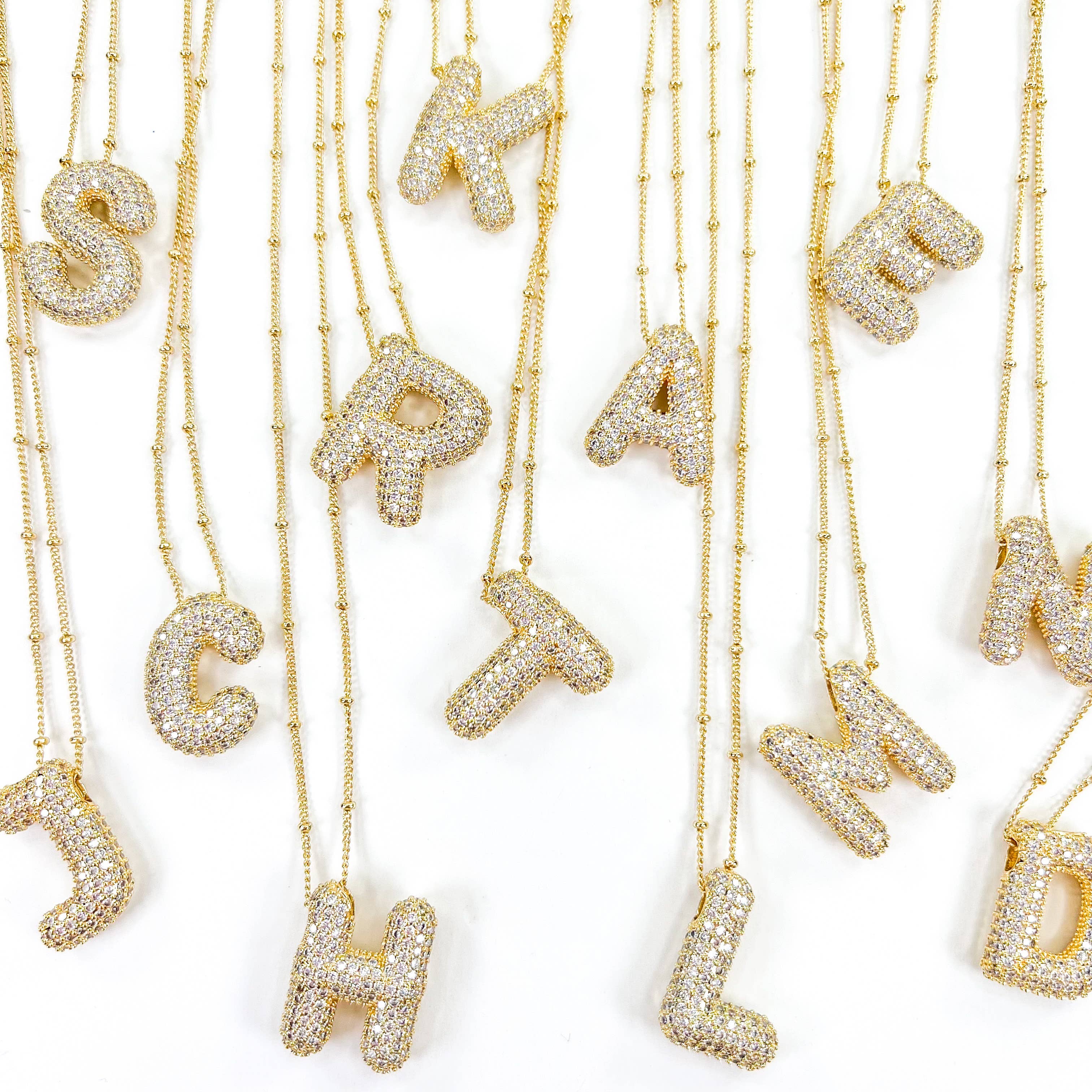 A collection of 18k gold balloon initial necklaces with bubble lettering, each embellished with cubic zirconia stones.