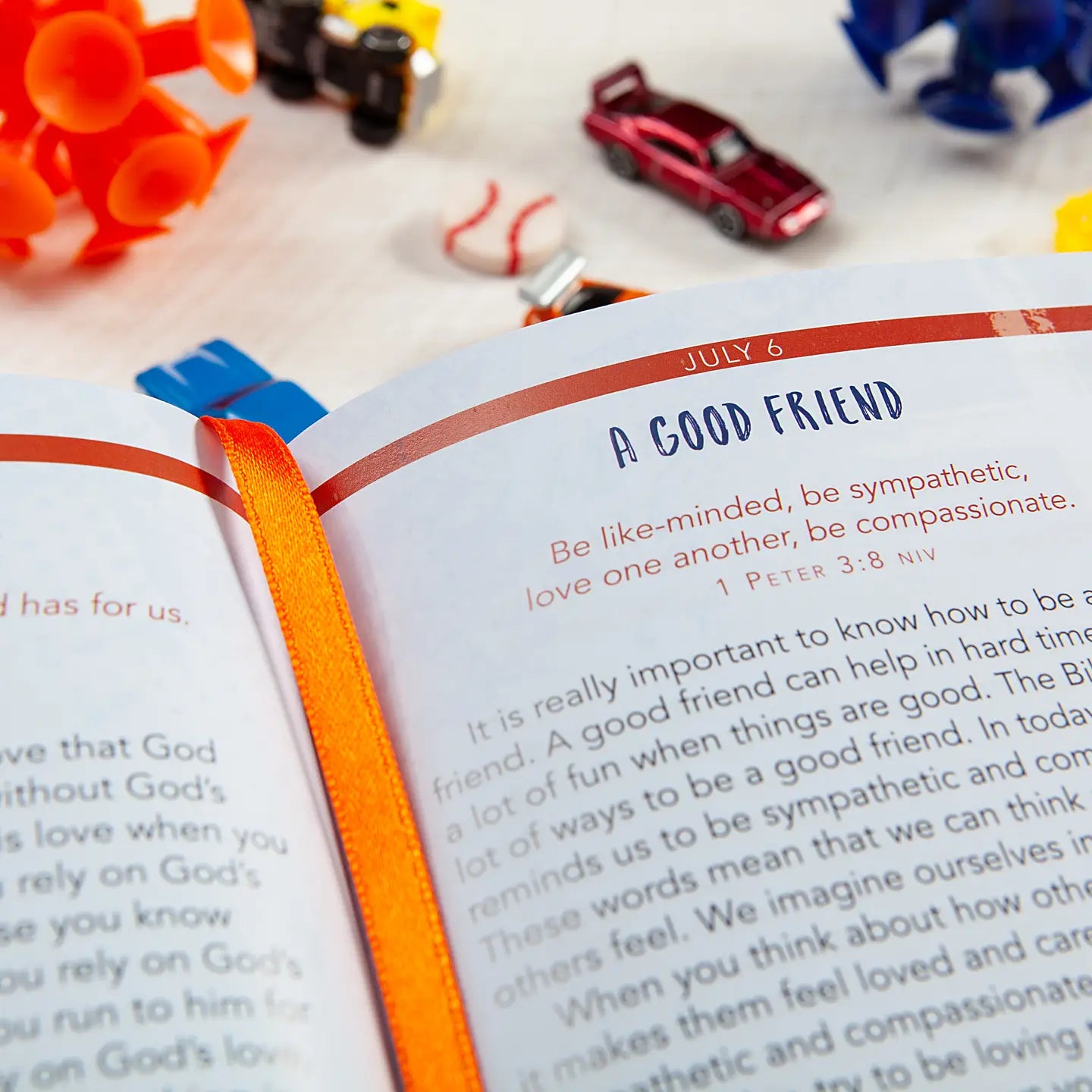 Devotional opened to a page zoomed in on the title "A Good Friend" laying on a white wooden surface surrounded by kids toys. 
