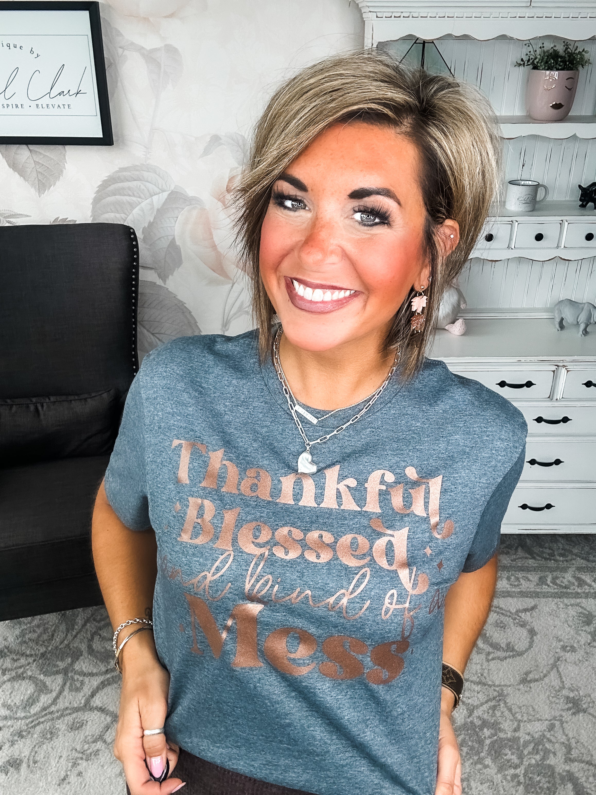 A woman wearing a grey t-shirt with the text 'Thankful Blessed and kind of a Mess' written in rose gold foil print.