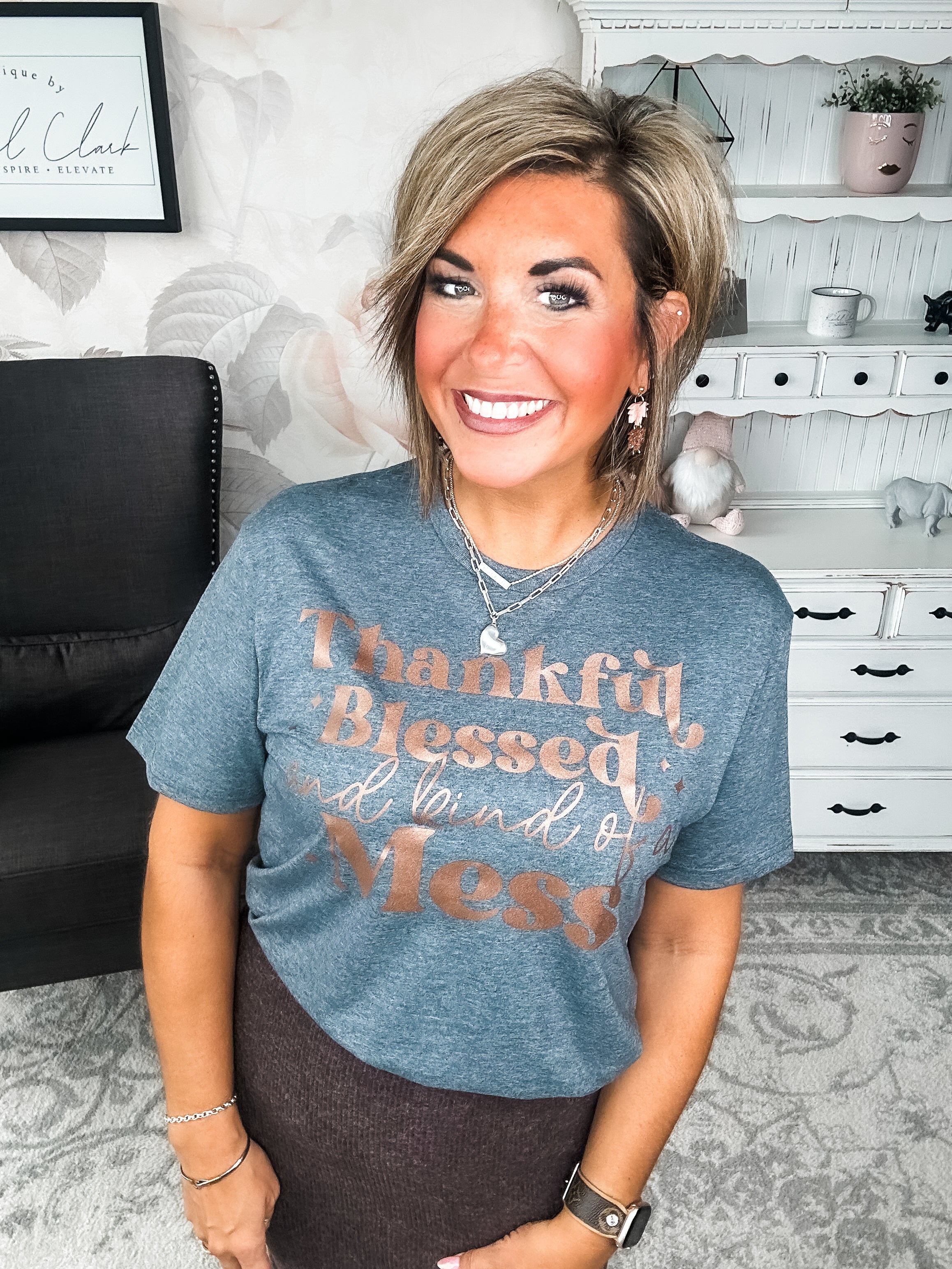 A woman wearing a grey t-shirt with the text 'Thankful Blessed and kind of a Mess' written in rose gold foil print.