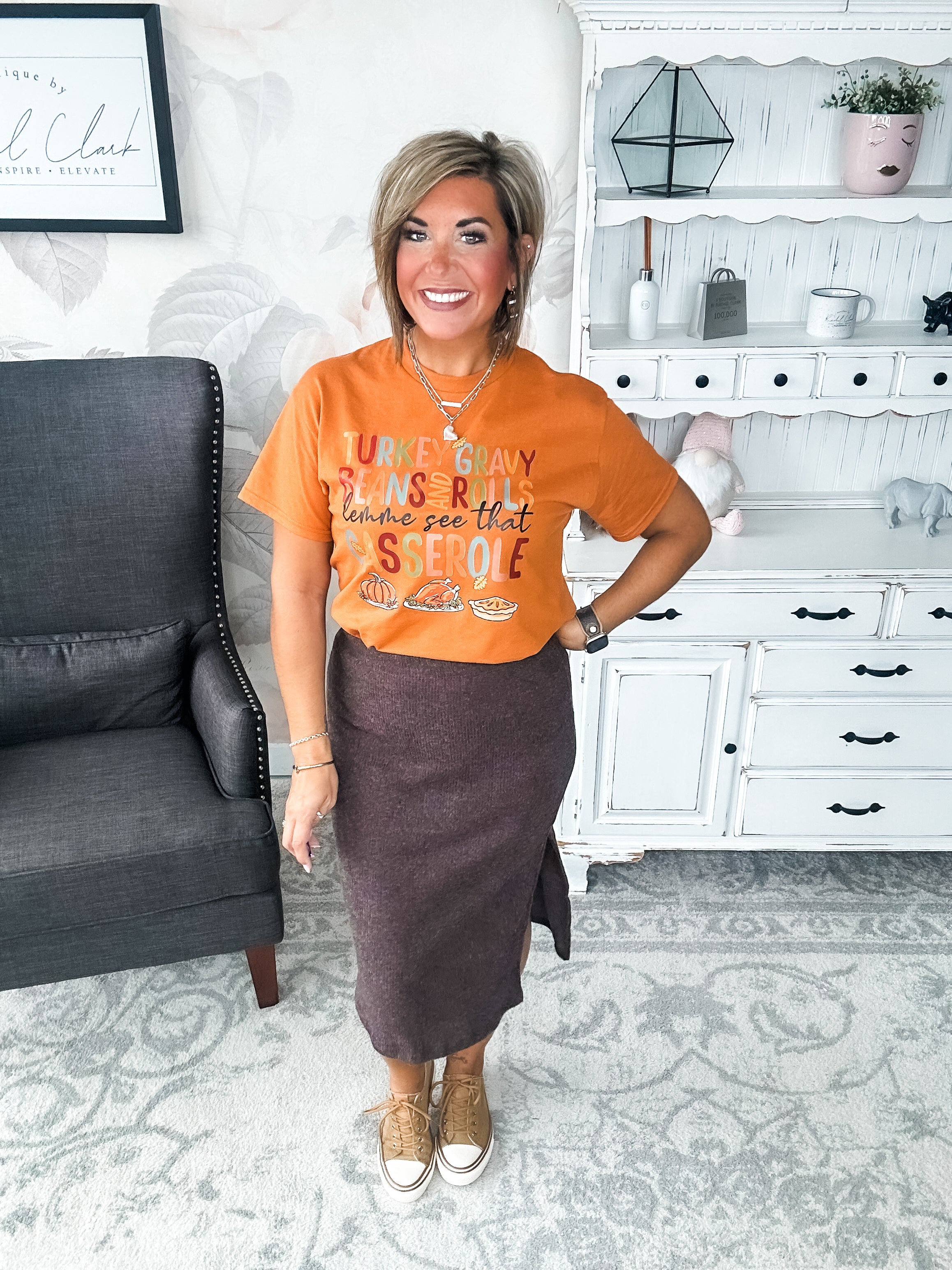 Woman wearing an orange t-shirt with Thanksgiving-themed text and graphics, that reads 'Turkey, gravy, beans and rolls, lemme see that casserole.'