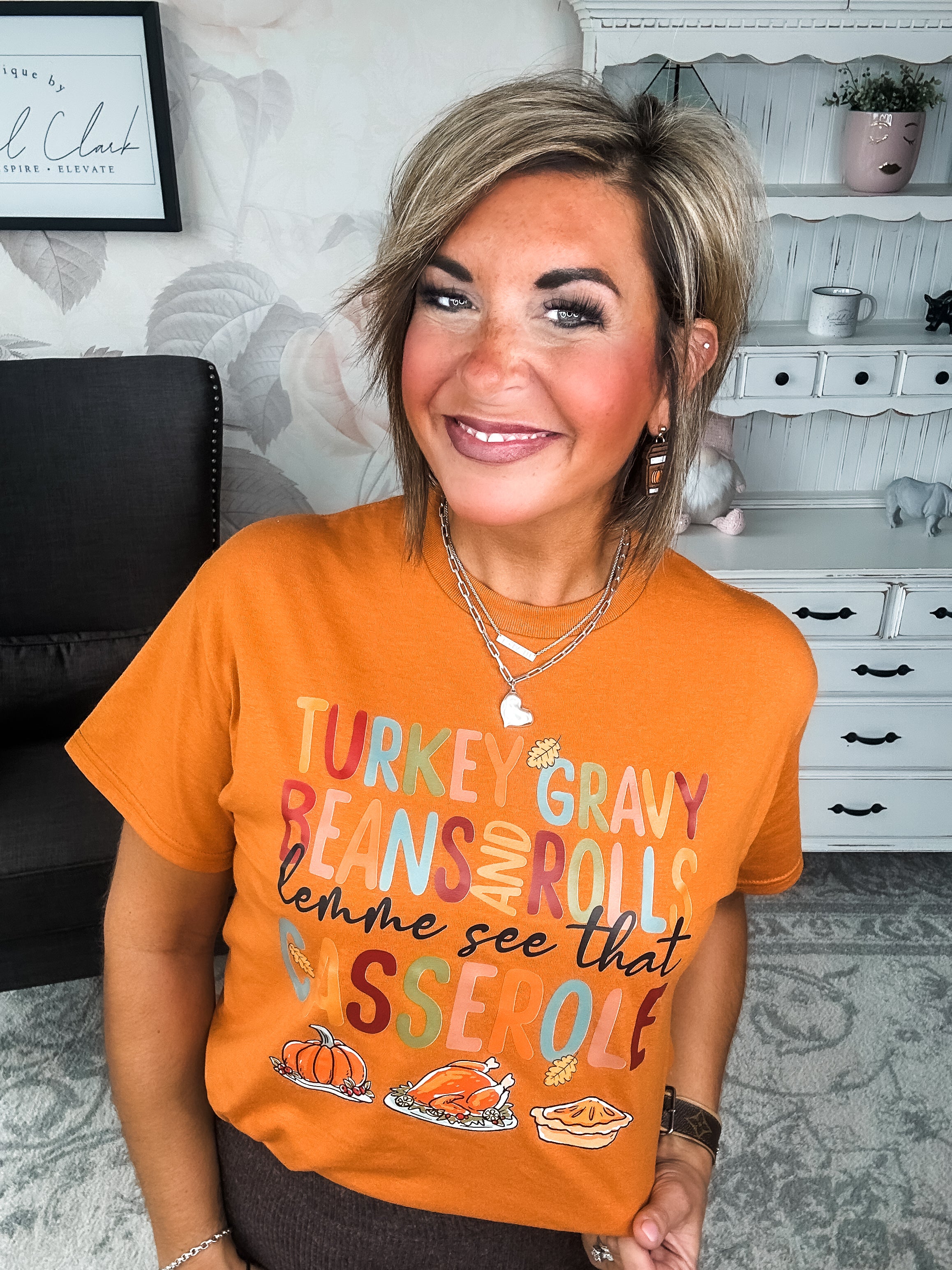 Woman wearing an orange t-shirt with Thanksgiving-themed text and graphics, that reads 'Turkey, gravy, beans and rolls, lemme see that casserole.'