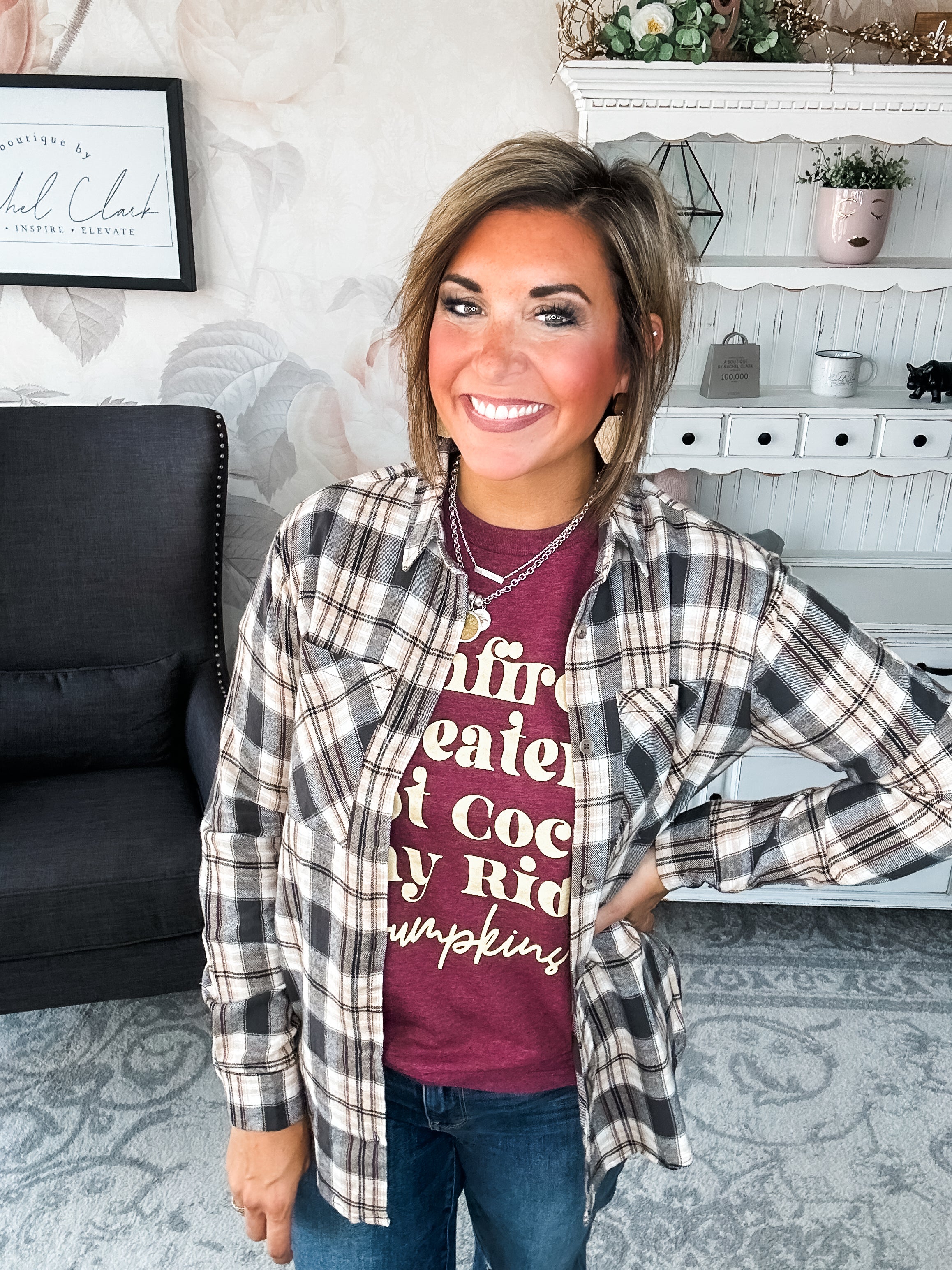 Woman wearing a maroon t-shirt that reads,  'Bonfires, Sweaters, Hot cocoa, Hay Rides and Pumpkins.' written in a cream text. 