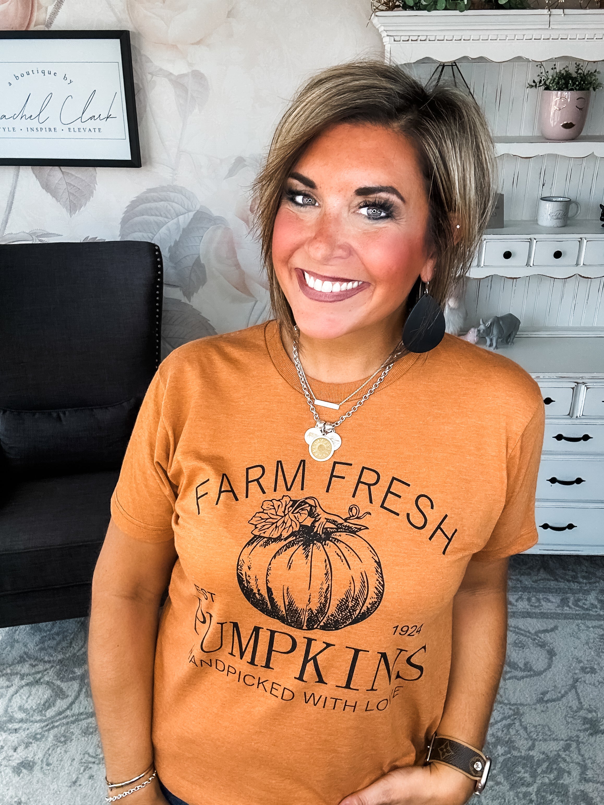 Woman wearing an orange t-shirt that says 'Farm Fresh Pumpkins, Handpicked with Love, Est. 1924' with a pumpkin graphic.