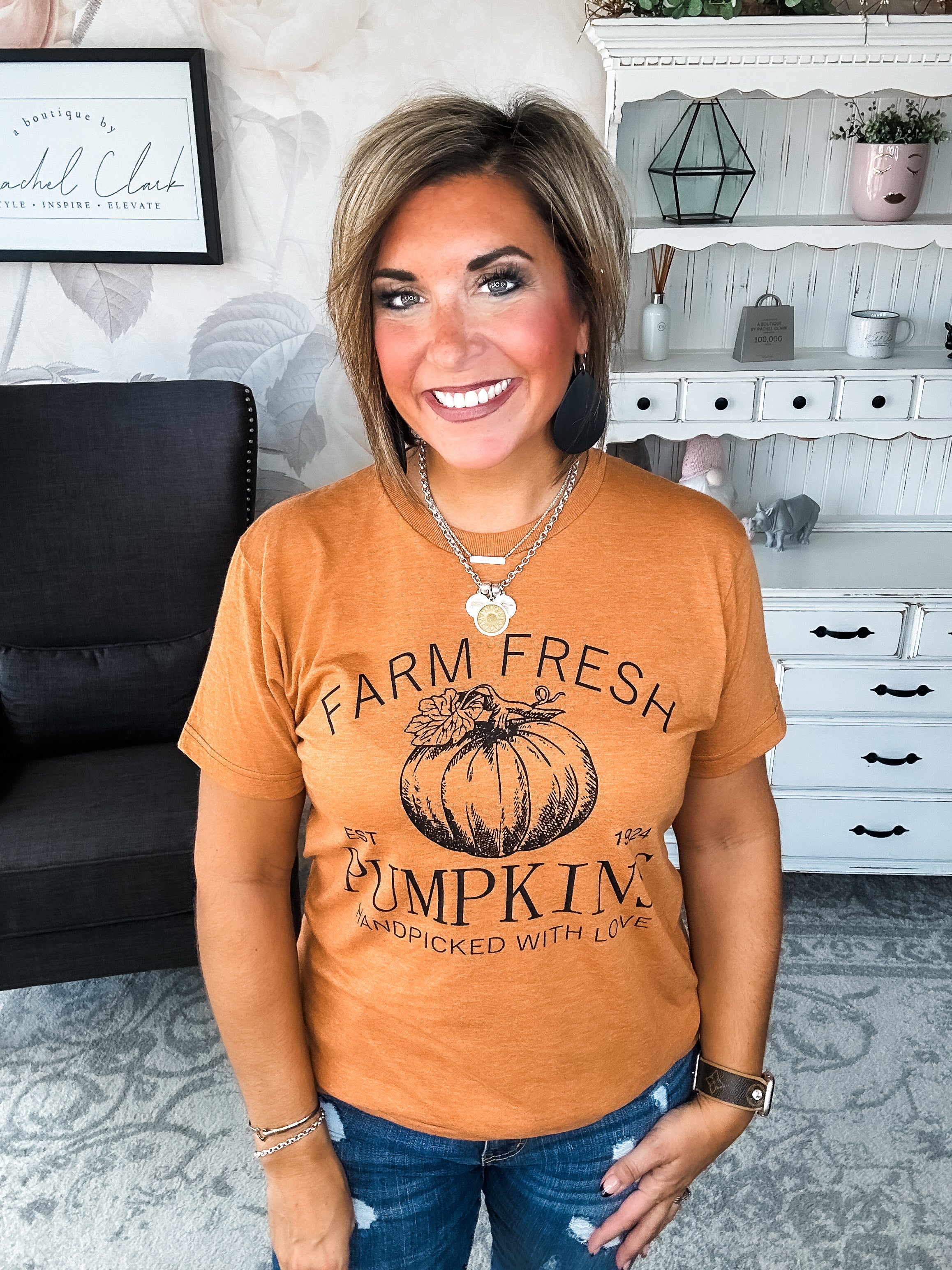 Woman wearing an orange t-shirt that says 'Farm Fresh Pumpkins, Handpicked with Love, Est. 1924' with a pumpkin graphic.